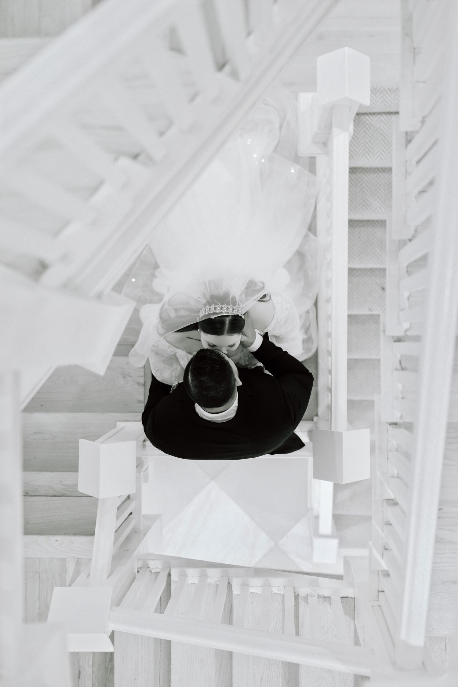 Black and white aerial view of a bride and groom embracing on white wooden stairs.