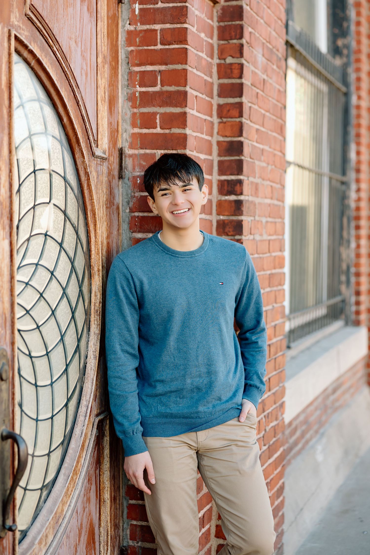 Casual portrait against red brick wall with vintage wooden door featuring circular design.