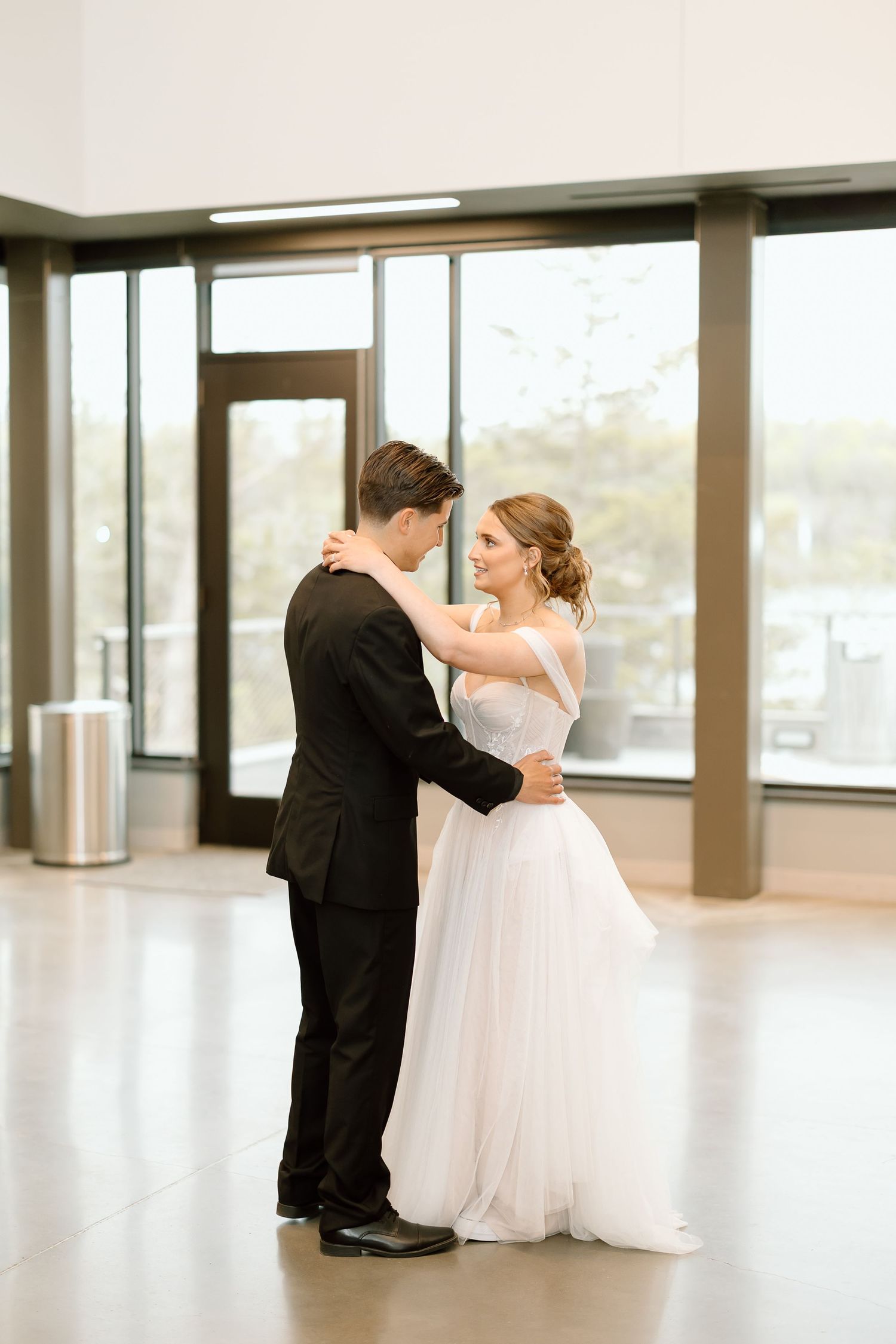 Couple shares first dance in modern venue with large windows.