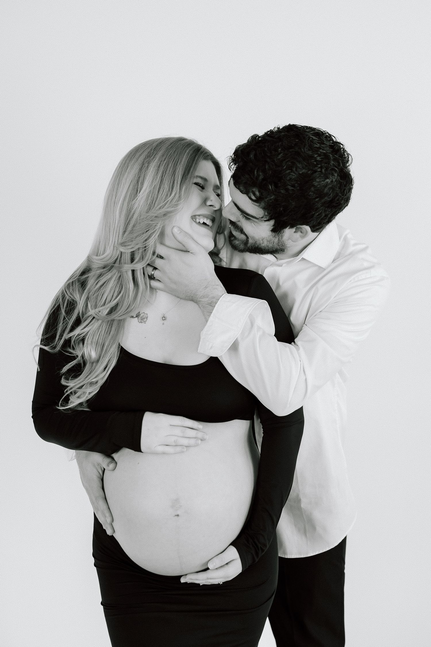 Black and white maternity portrait capturing couple's laughter.