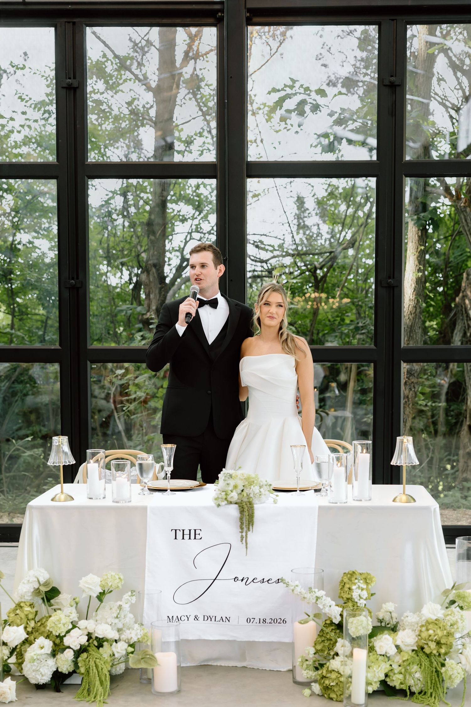 Elegant wedding couple at sweetheart table with white floral arrangements and The Joneses personalized banner.