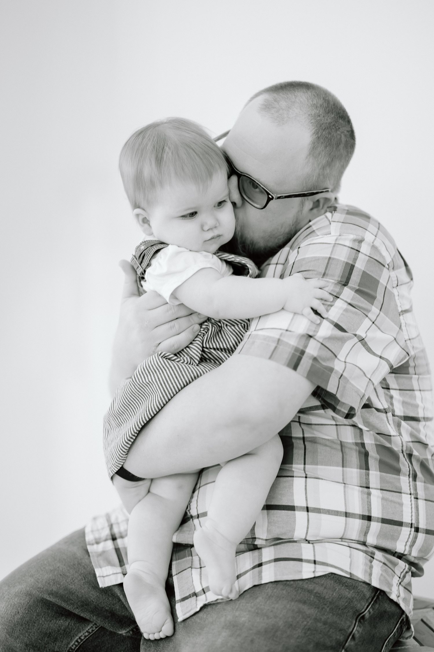 Black and white photo series showing tender moments between an adult in plaid shirt holding and embracing a small baby.