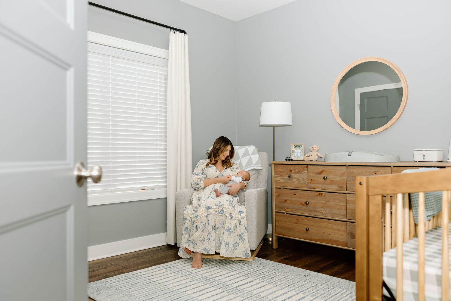 Modern nursery room with white walls, wooden crib, and floral wallpaper accent wall features natural decor elements.