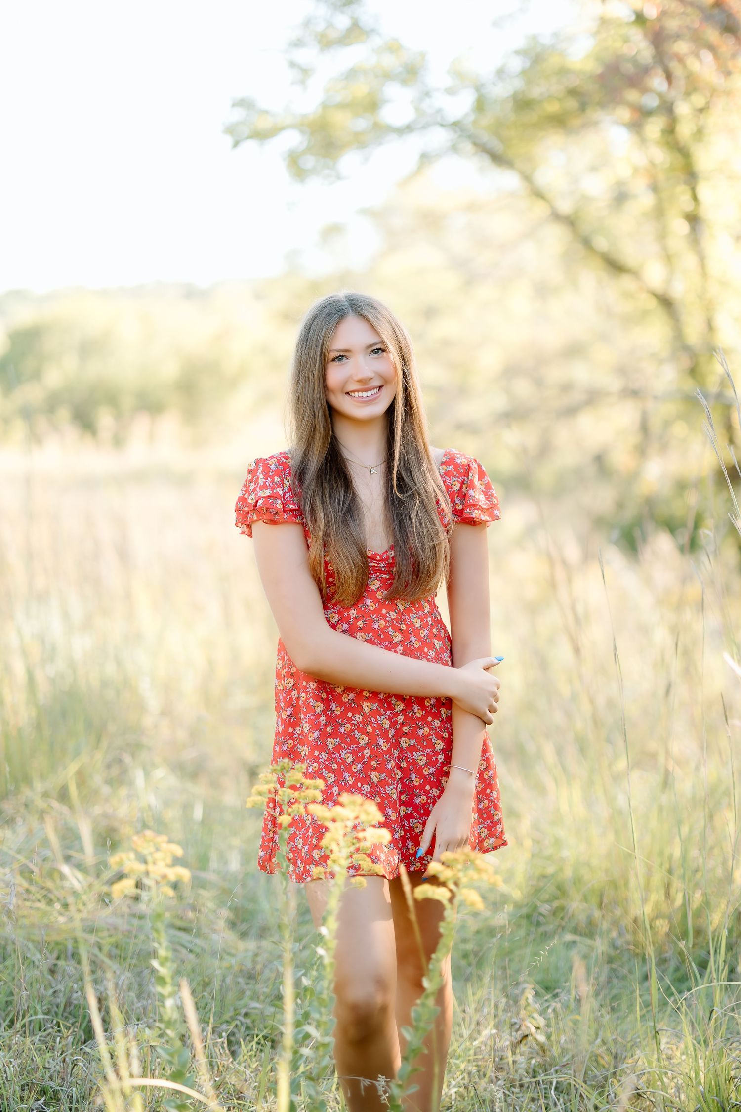 A person in a red floral dress stands in a sunlit meadow with tall grass and soft golden light in the background.