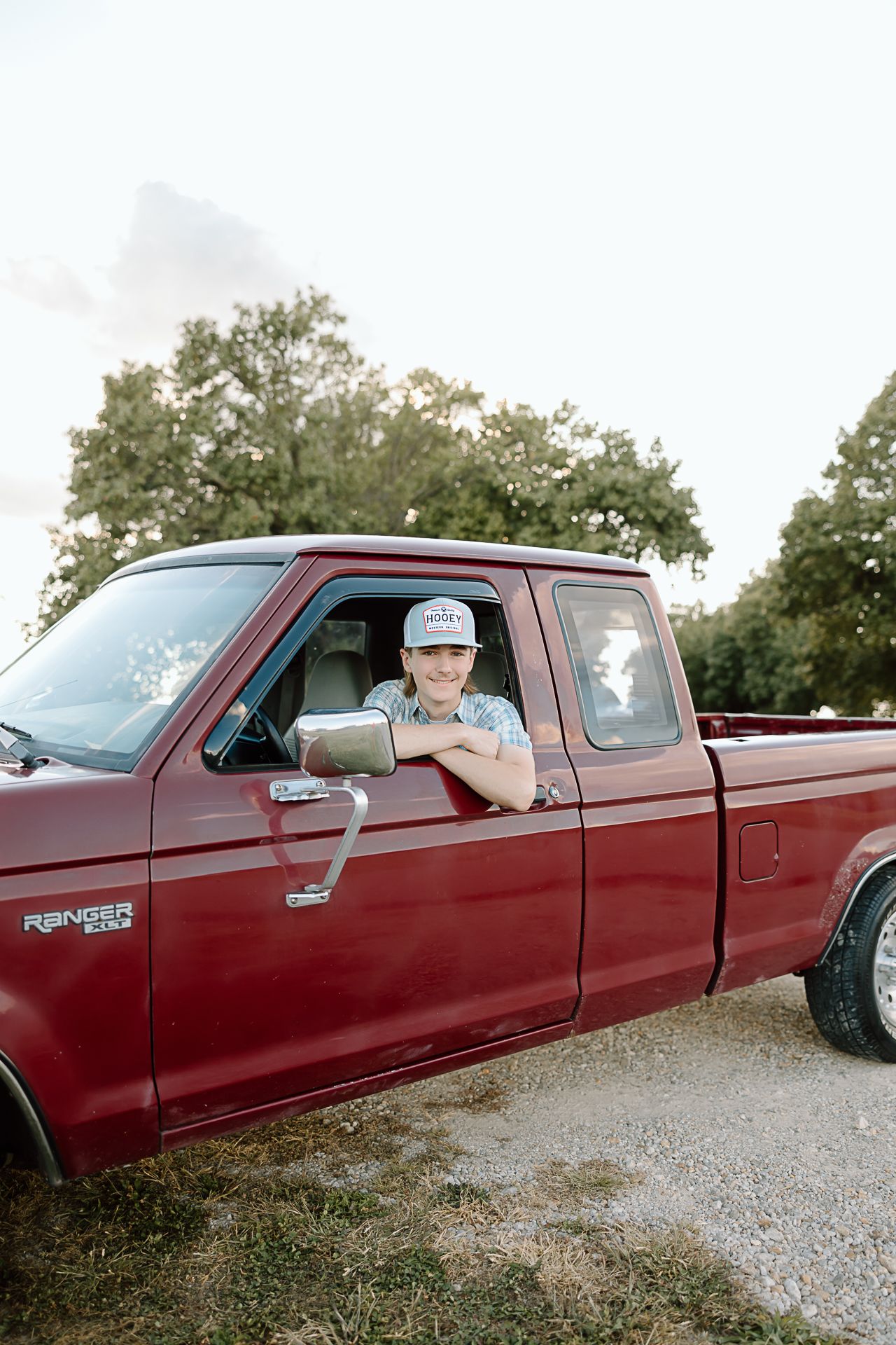 A red extended cab pickup truck parked on a gravel road with trees in the background.