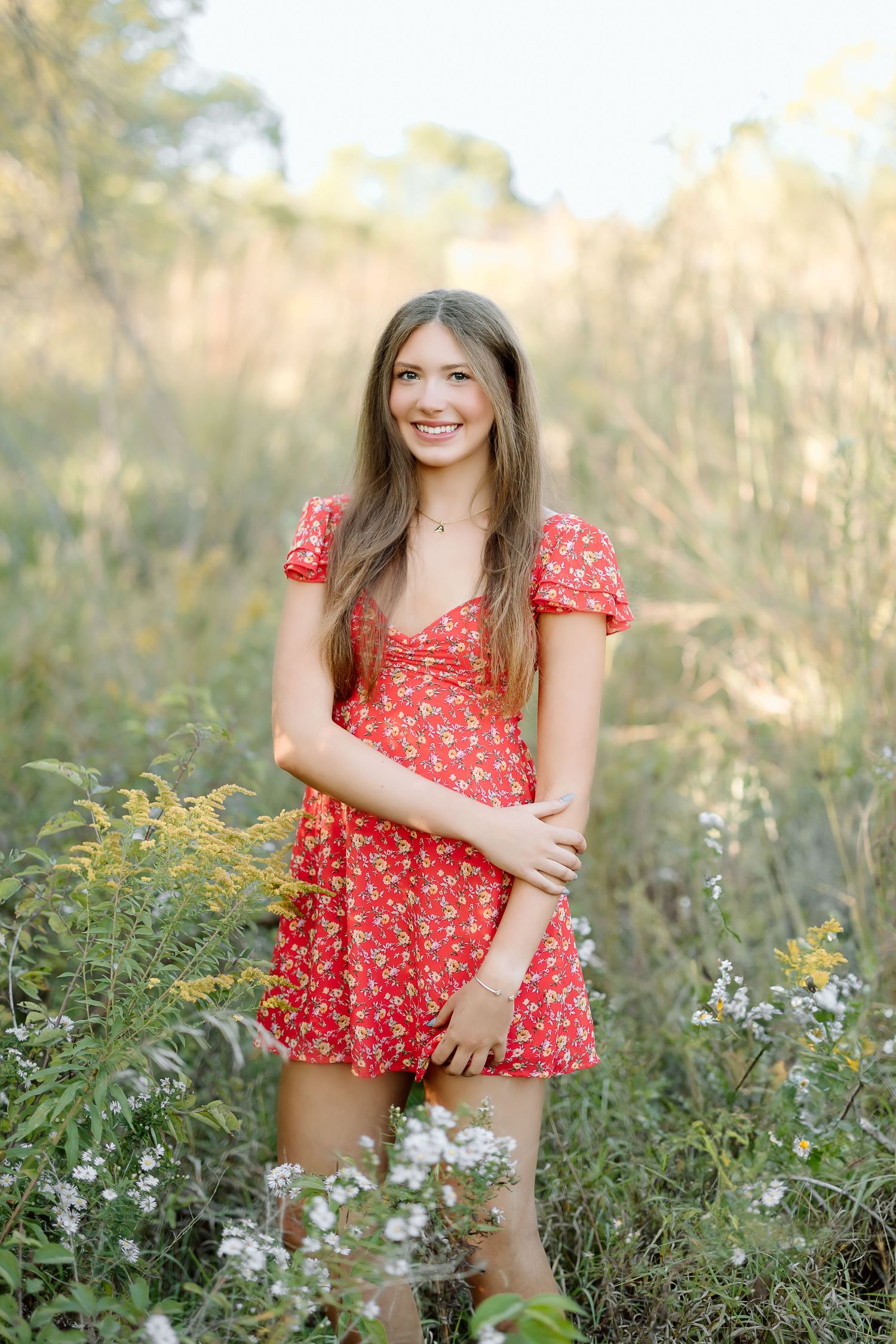 A person in a red floral dress poses outdoors in a wildflower meadow during golden hour.