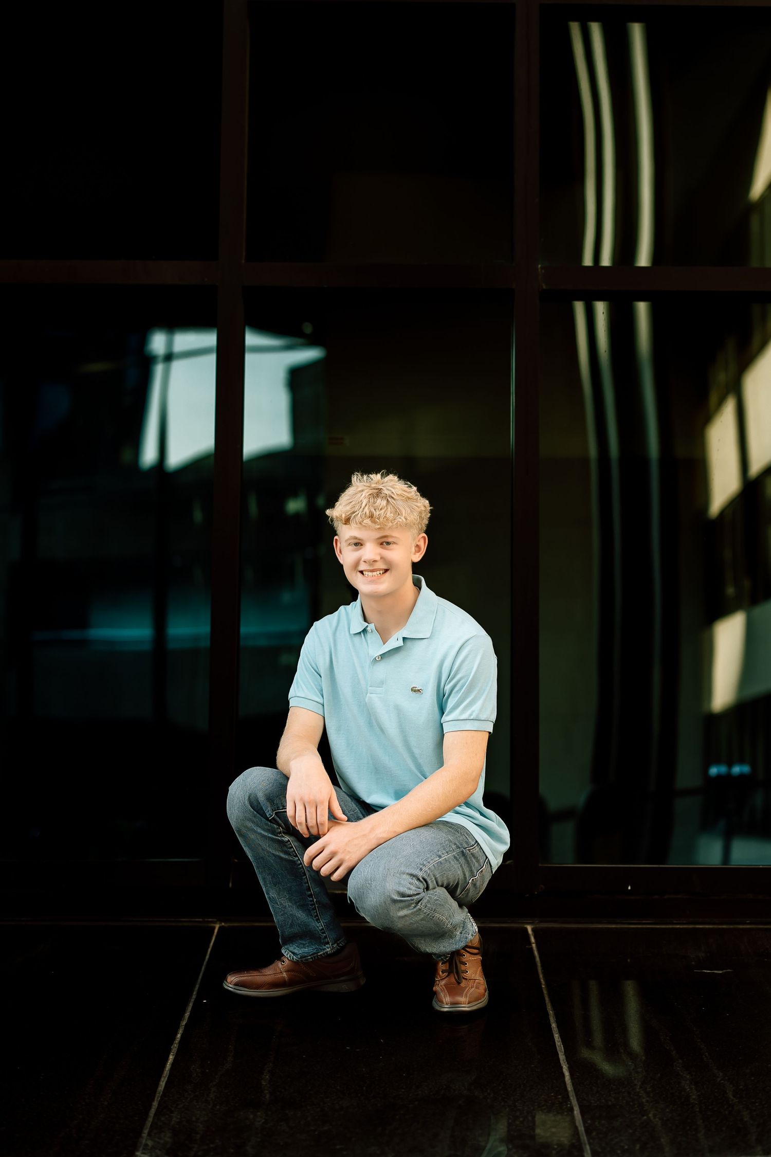 Person in light blue polo shirt sitting casually against dark background in artistic portrait series.