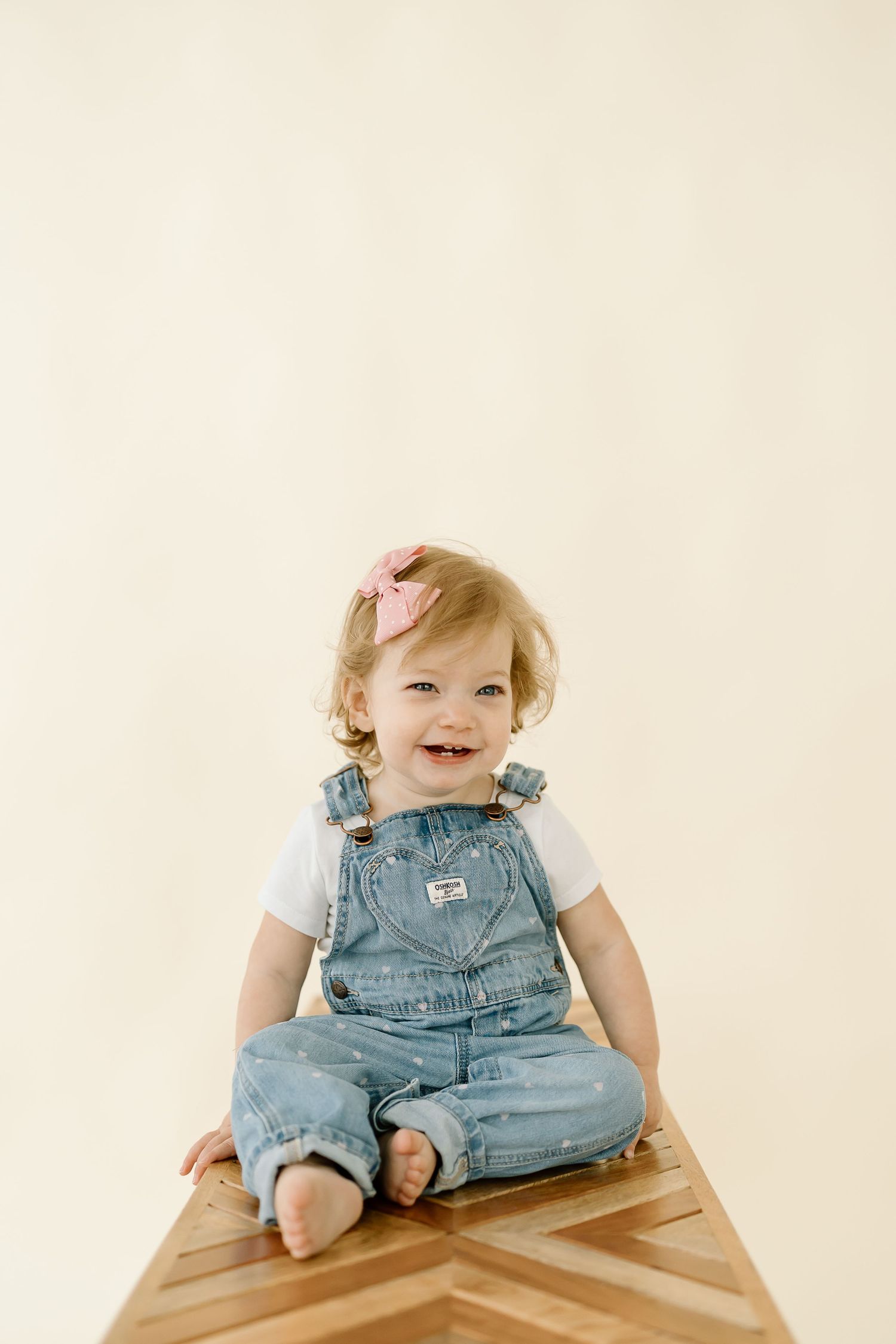 A series of four photos showing a toddler in denim overalls sitting on a wooden surface in different poses.