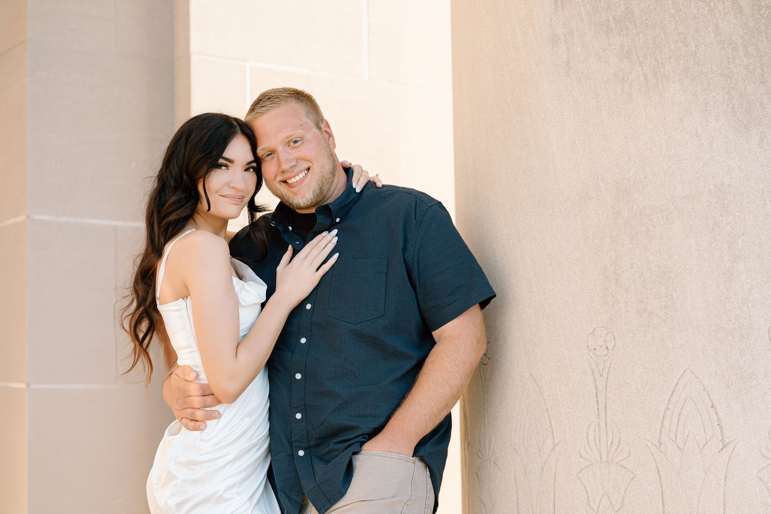 A couple in casual attire shares intimate moments in a series of romantic poses against a neutral wall.
