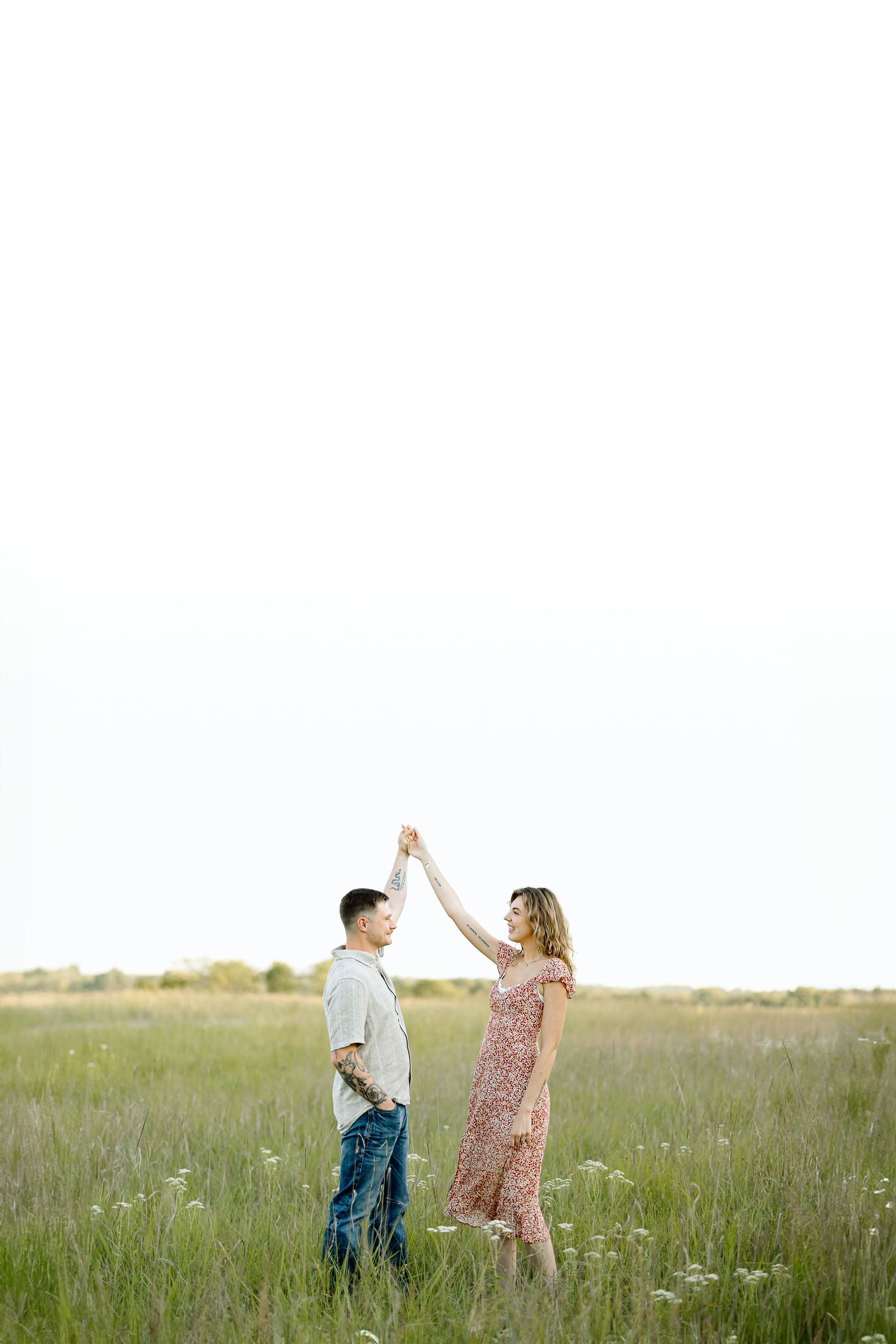 A couple dances together in a sunlit meadow filled with wildflowers during golden hour.