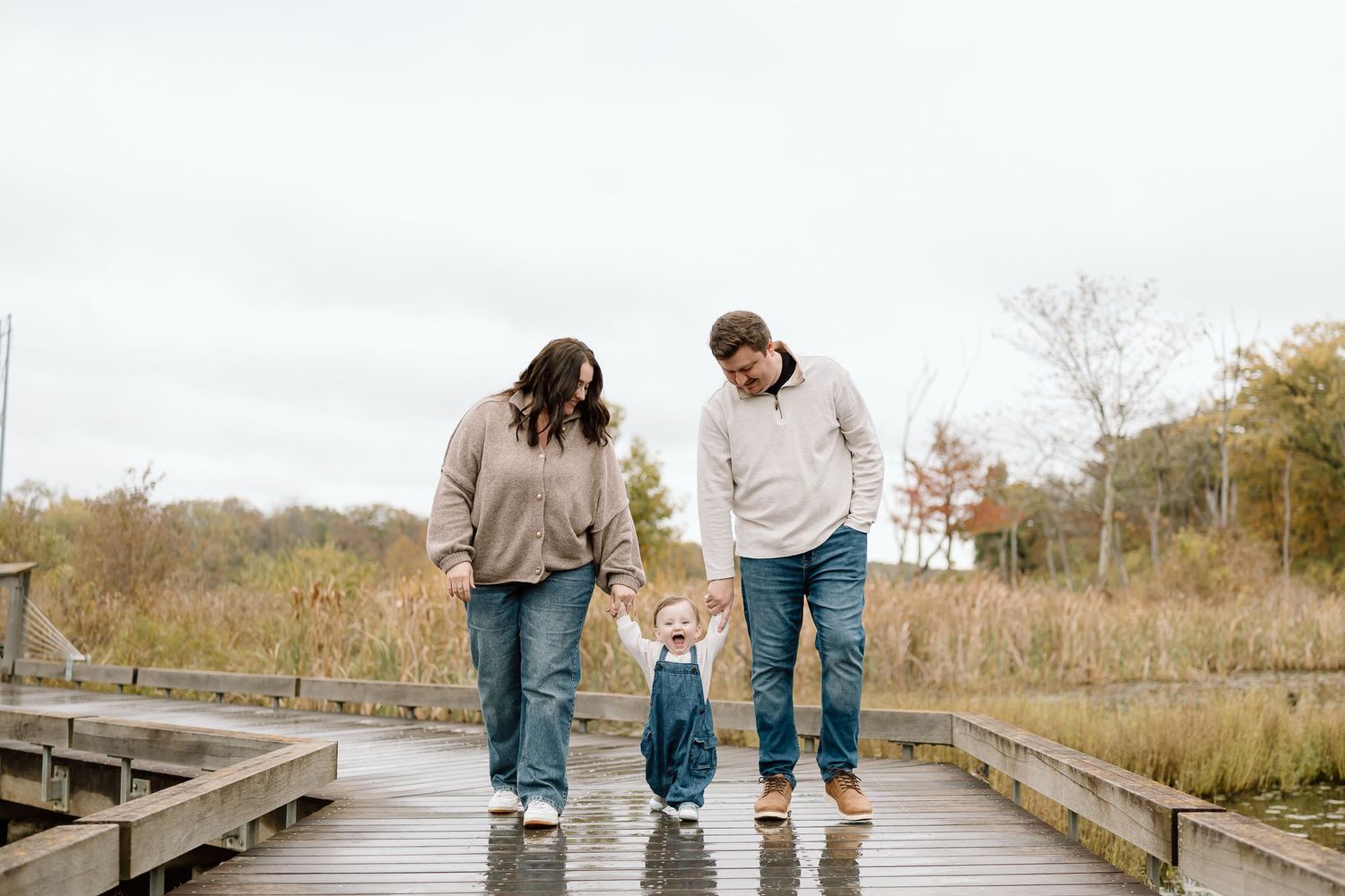 A group of people walk together on a wooden boardwalk through a natural area during autumn.