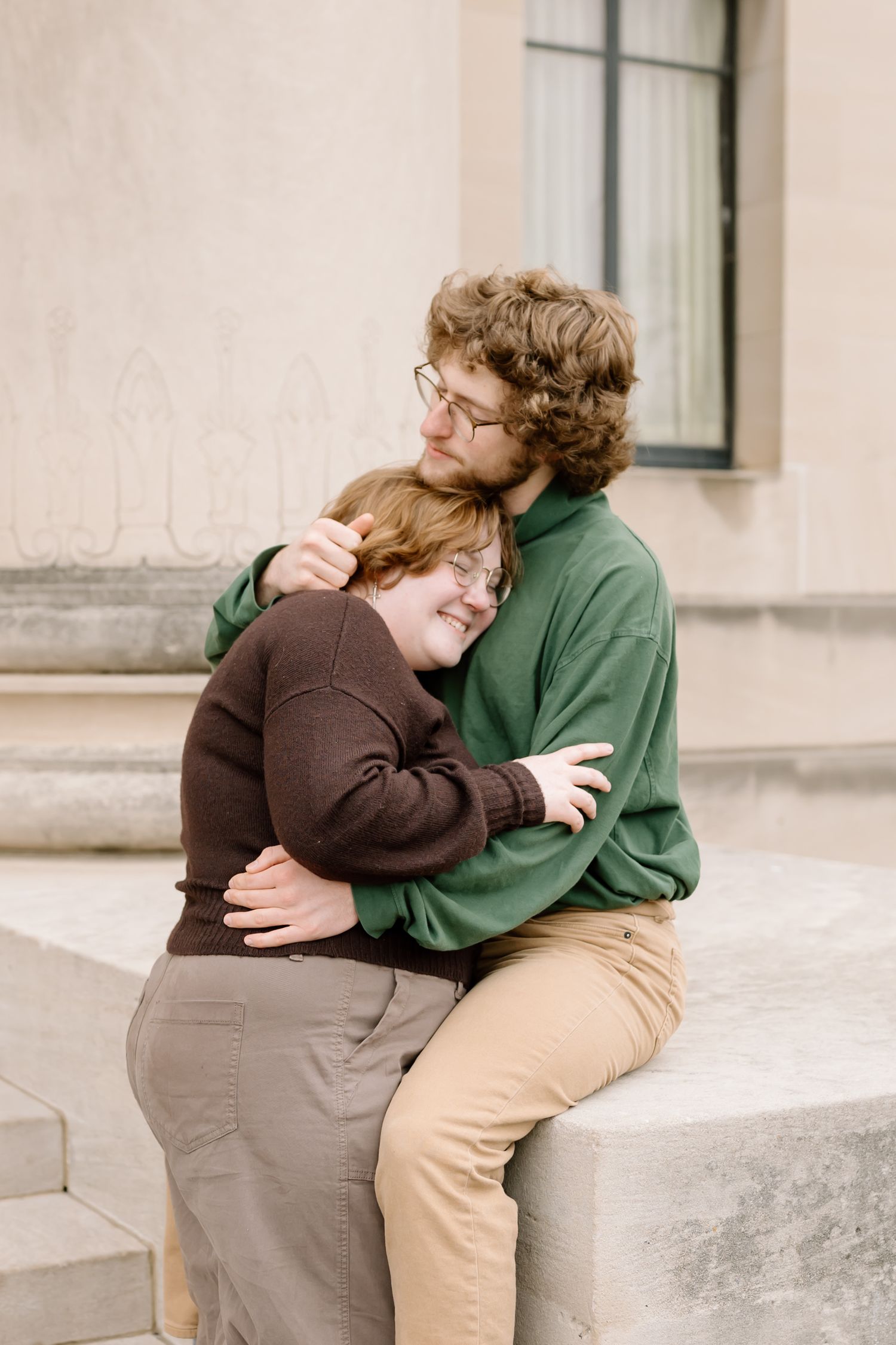 Two people in brown and green clothing share an intimate moment sitting together on concrete steps.