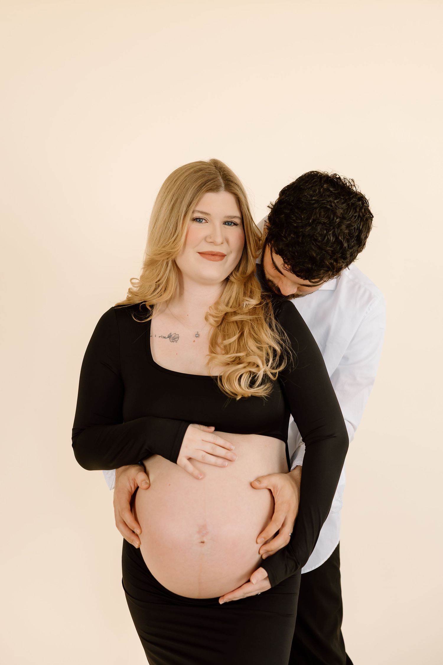 Maternity photo series showing a pregnant woman in black dress with partner embracing her growing belly.