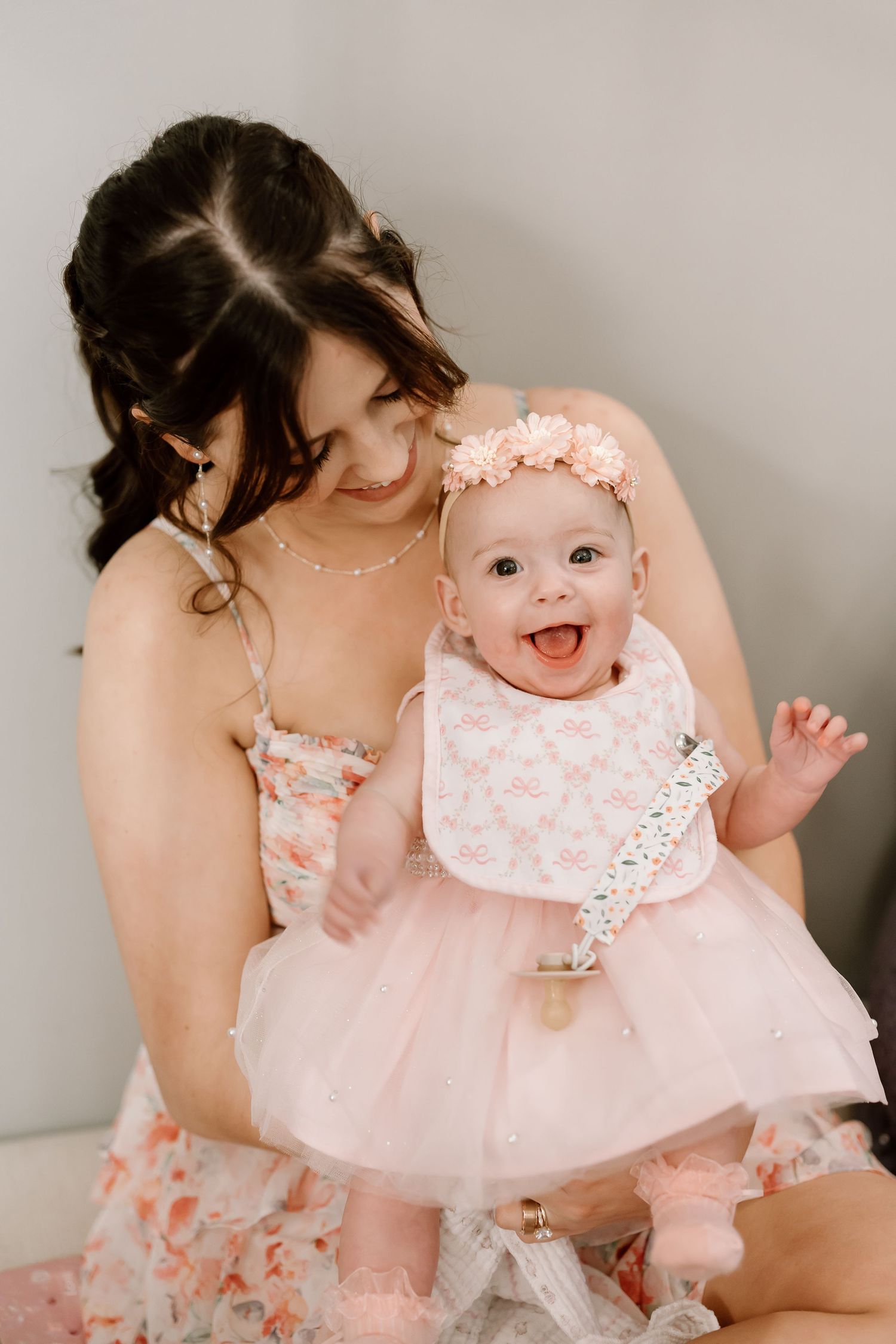 Baby wearing pink dress and lace bib smiles joyfully while being held in series of connected portrait photos.