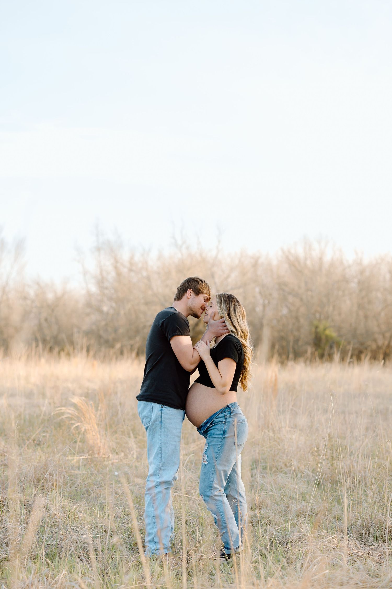 A romantic couple embraces in a golden field of tall grass during sunset.