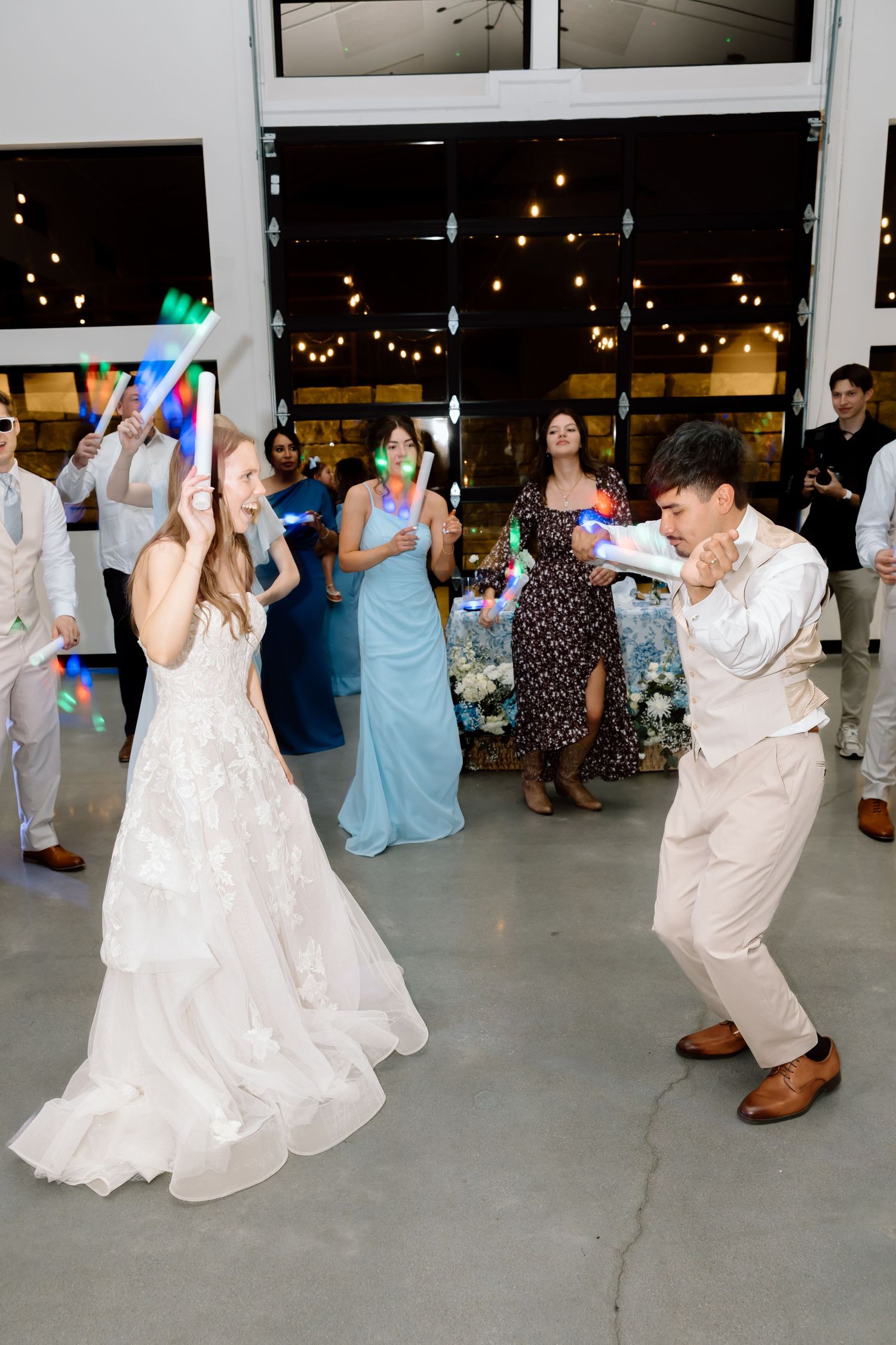 Bride and groom dancing with glow sticks at their wedding reception, surrounded by guests celebrating.