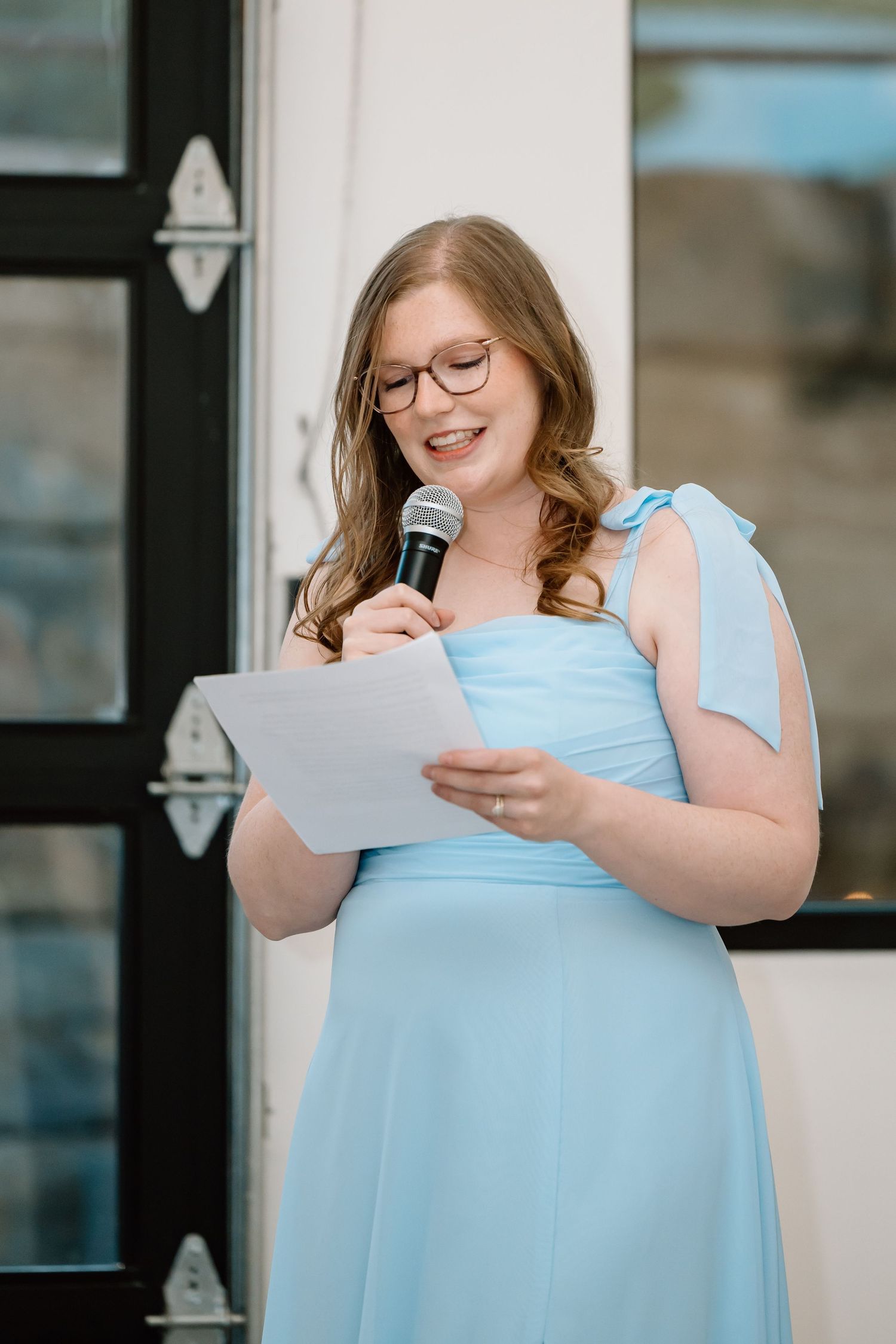 Bridesmaid in light blue gown delivering a heartfelt speech with microphone at a wedding reception.