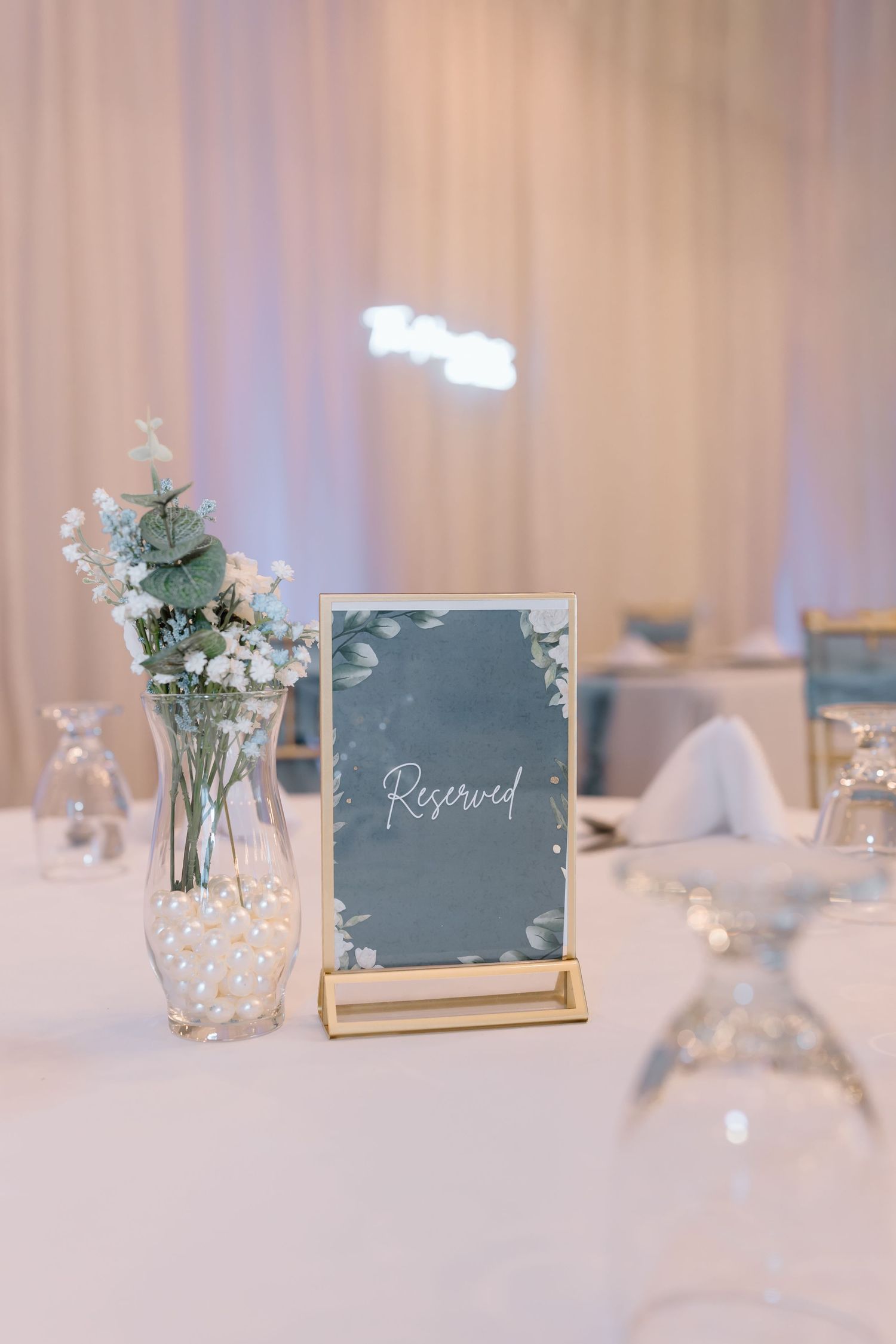 Elegant wedding table setting with a reserved sign in gold frame and delicate floral centerpiece in crystal vase.