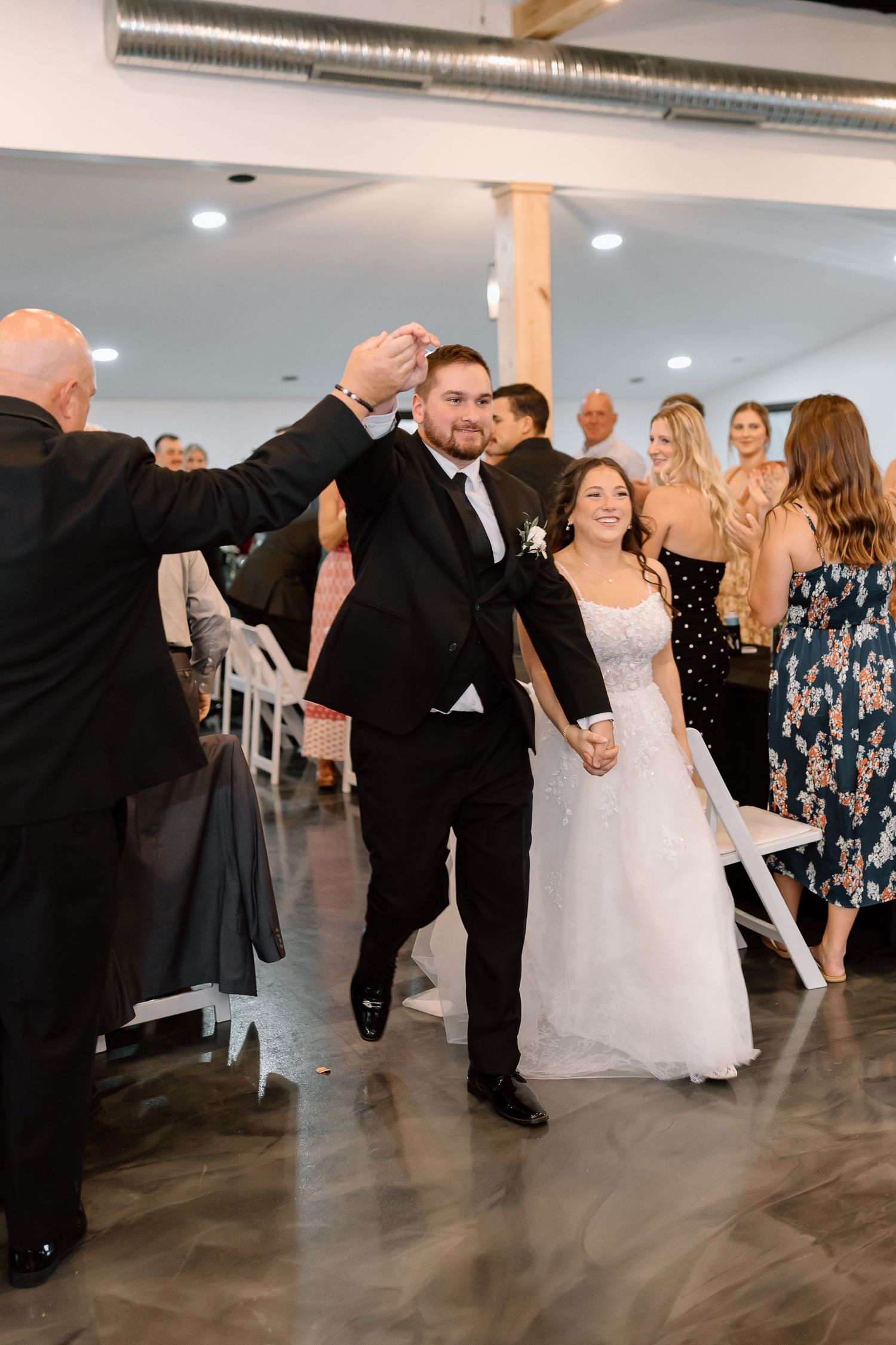 Wedding guests dance together at a reception in a modern venue with gray floors and white walls.