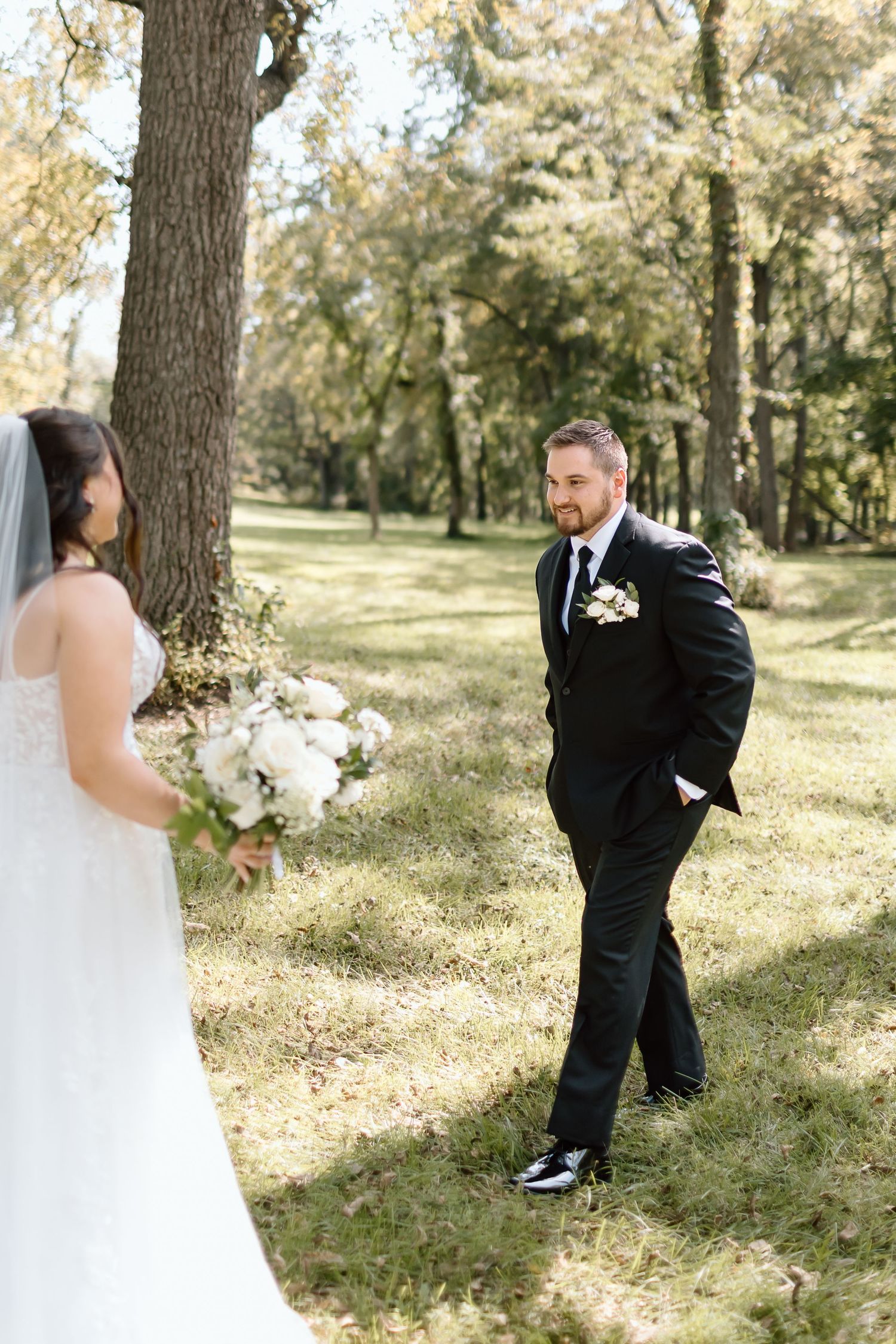 A romantic first look sequence between bride and groom in a sunlit wooded area during their wedding day.