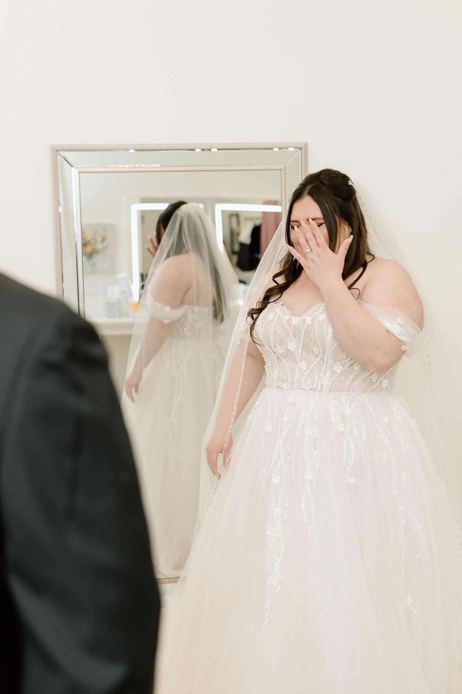 An emotional moment as someone tries on a beautiful white lace wedding gown while looking in a mirror.