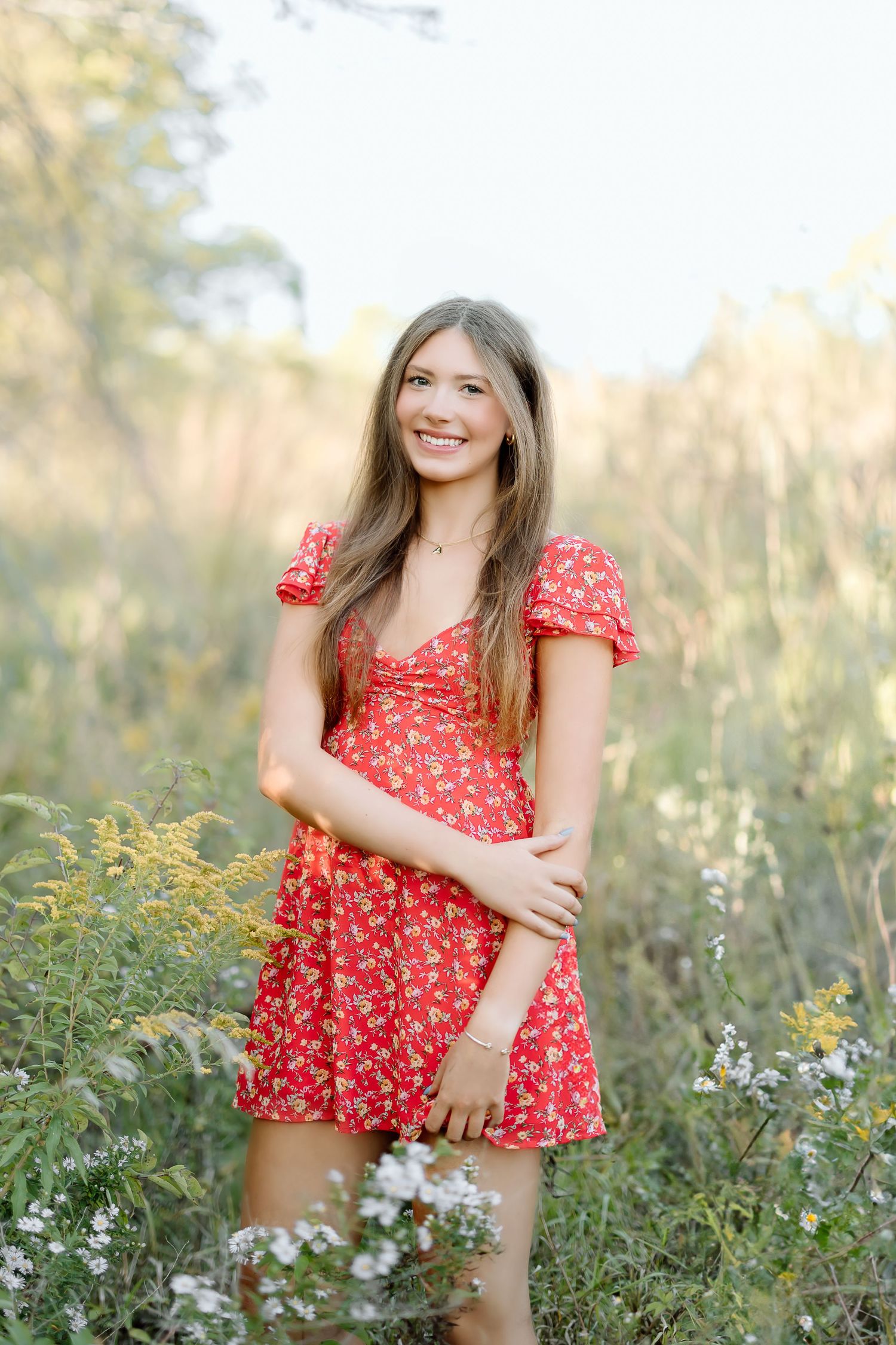 A red floral summer dress stands out against a soft natural meadow background in warm evening light.