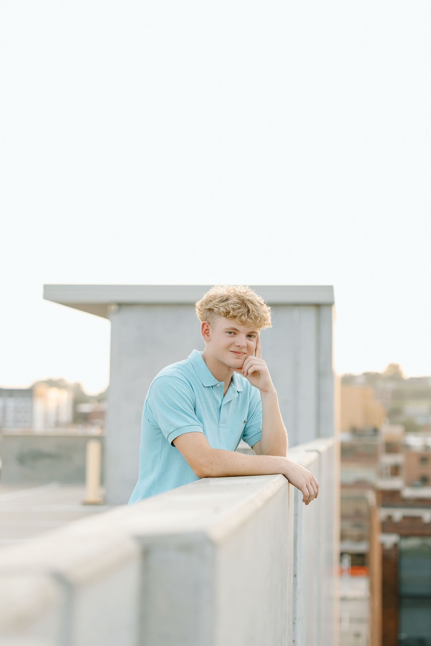 A person in a light blue polo shirt poses outdoors against a railing during a photo session.