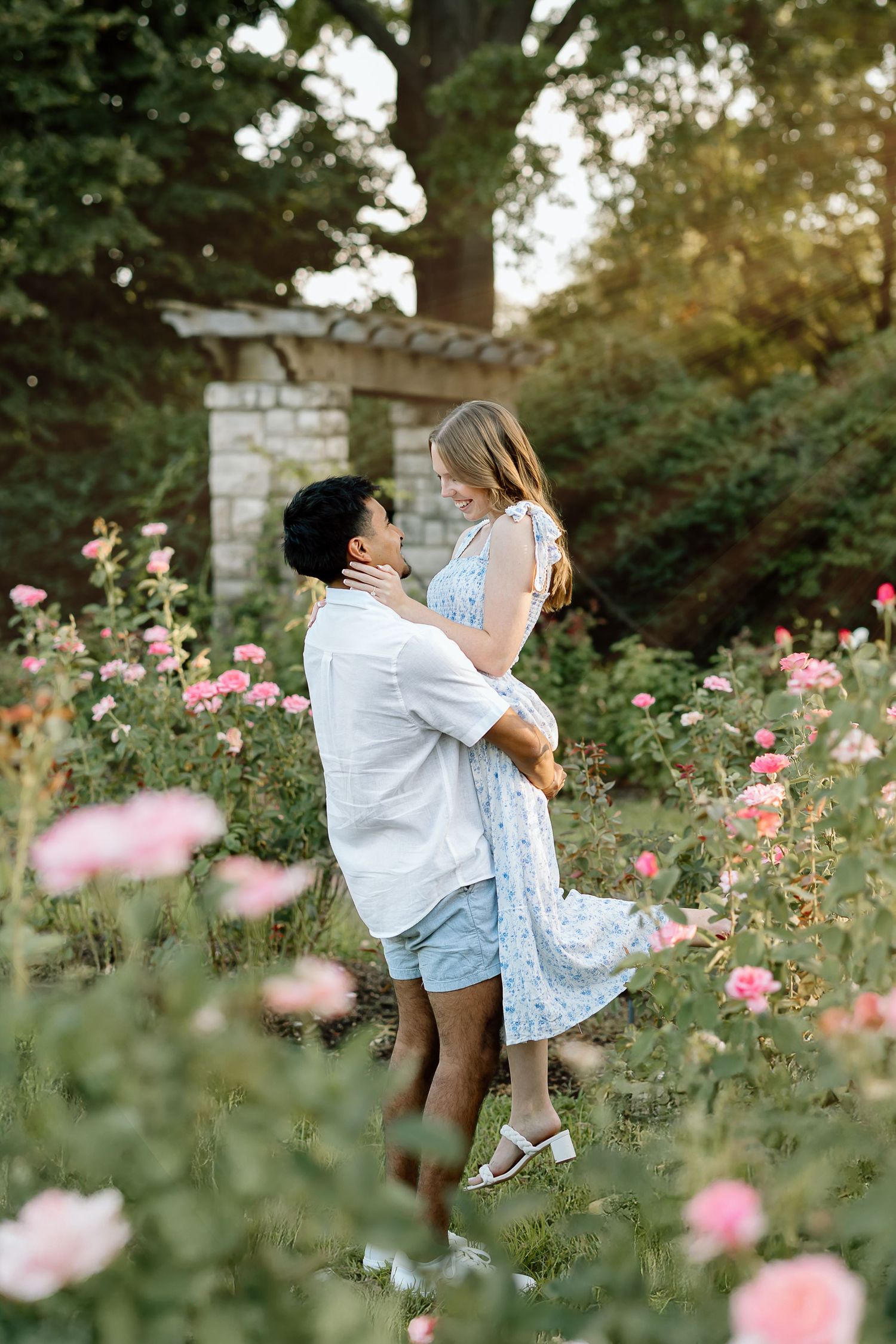A couple shares a romantic moment in a blooming rose garden during sunset.
