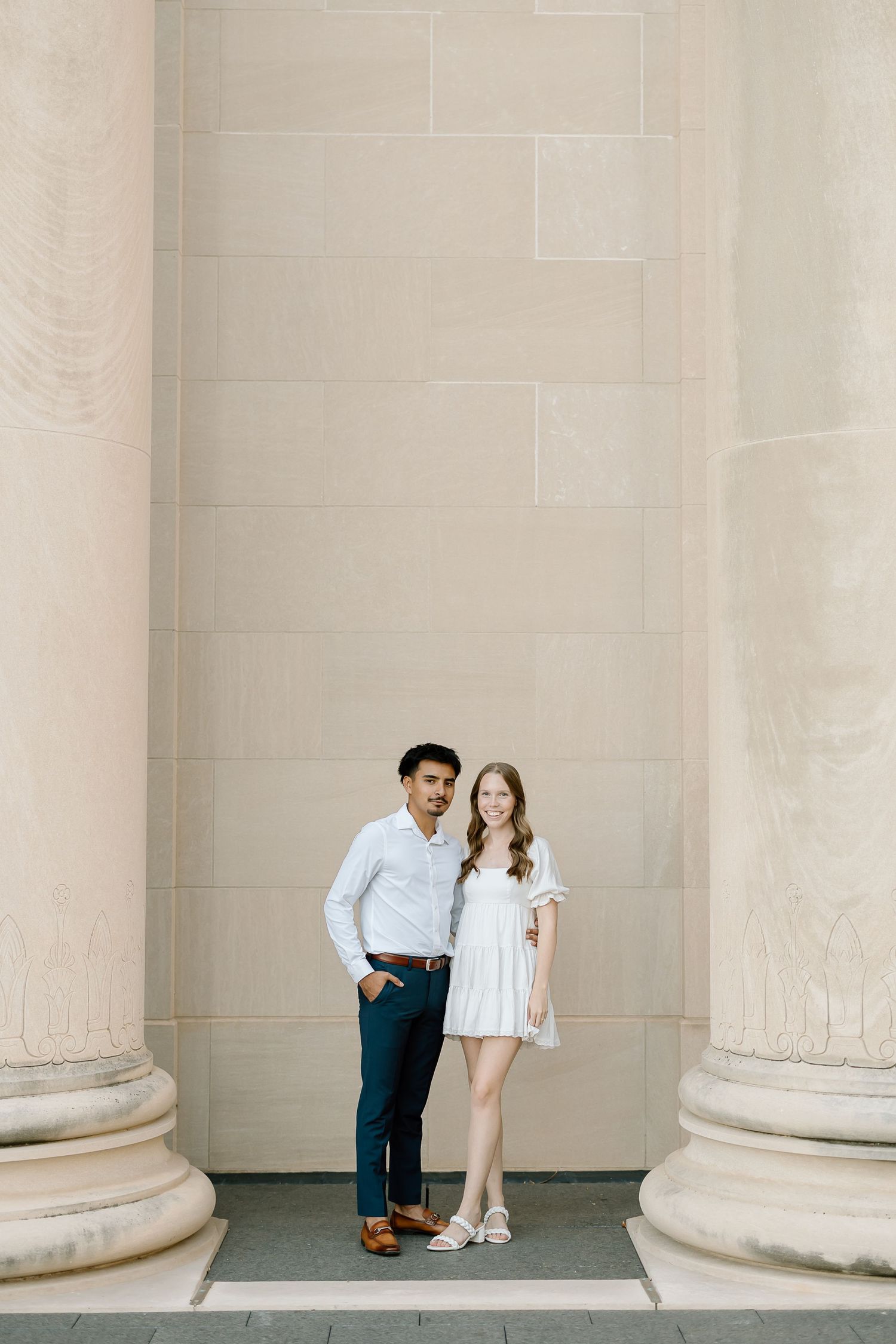 A couple poses together between elegant stone columns in a series of romantic architectural photos.