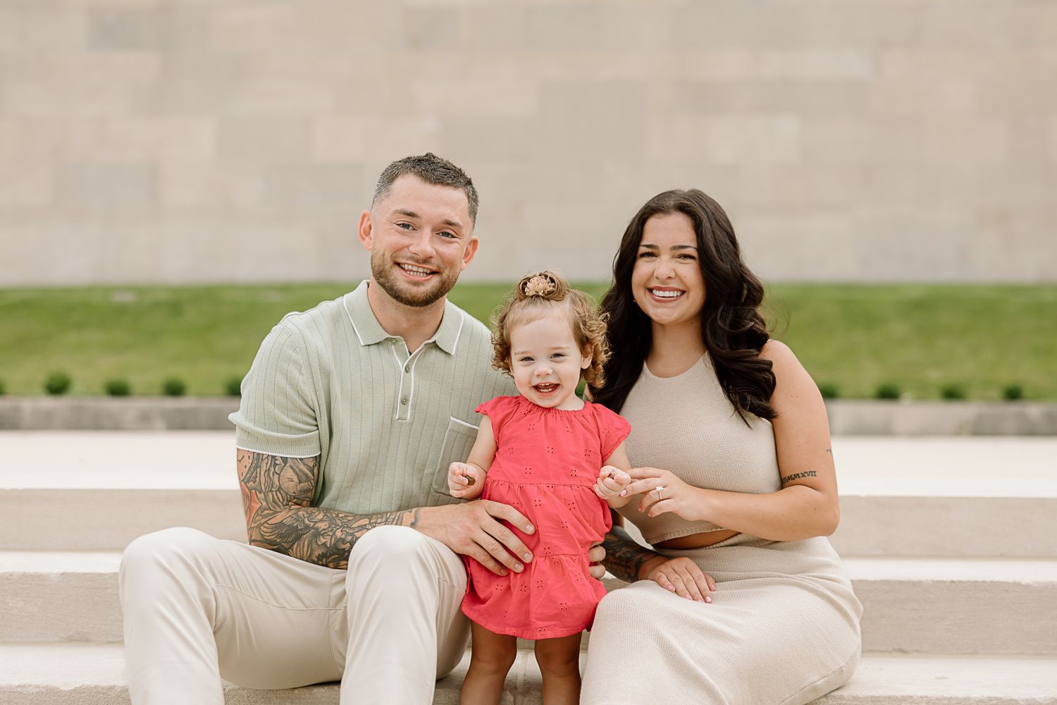 Family sitting together on outdoor concrete steps wearing coordinated beige and coral outfits.