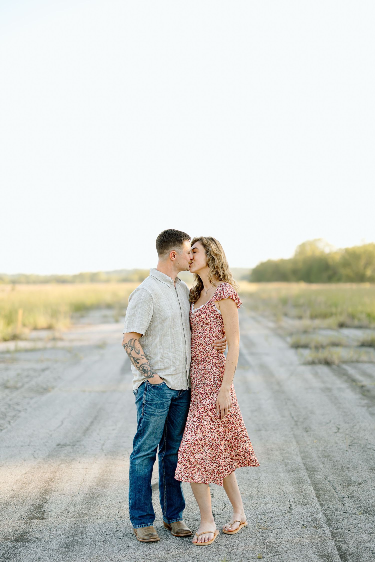 A couple shares an intimate moment on a dirt road at sunset in a romantic countryside setting.