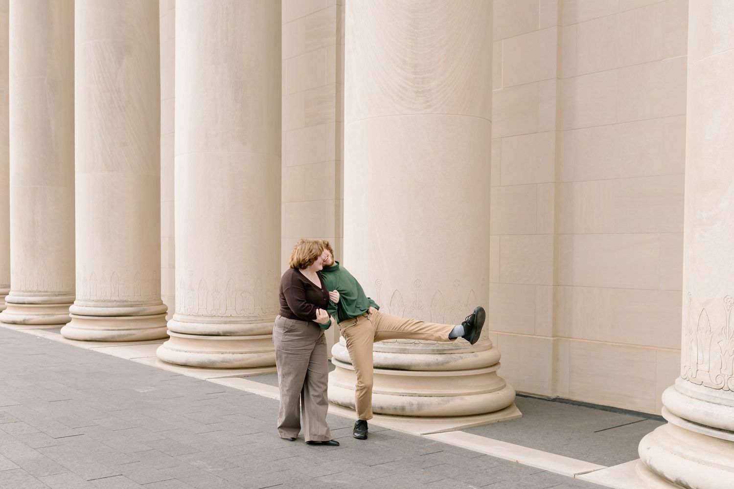 Romantic couple embracing between classical white columns in sunlight.