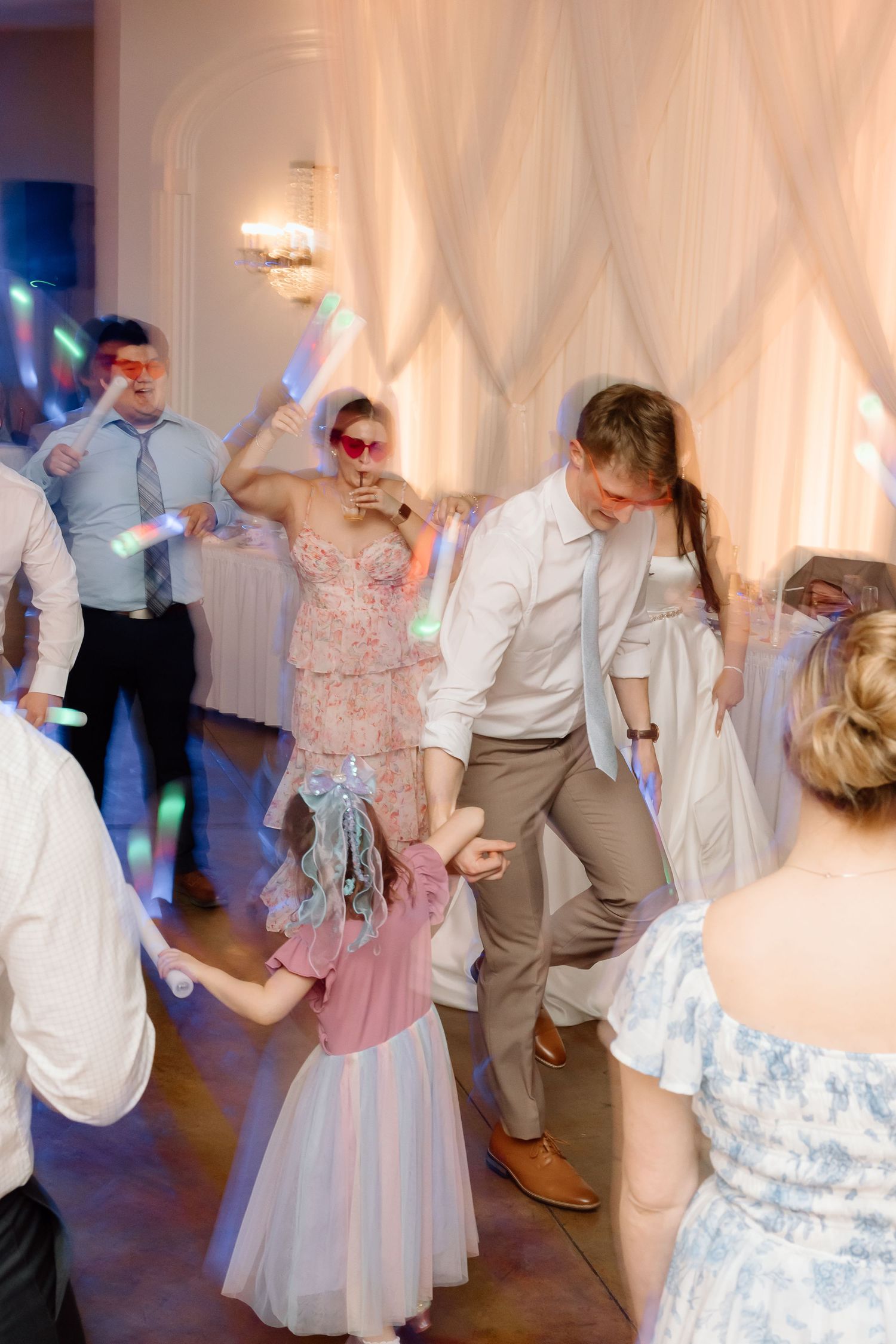 Wedding guests dance and celebrate on a white-draped dance floor with colorful lighting at an elegant reception.
