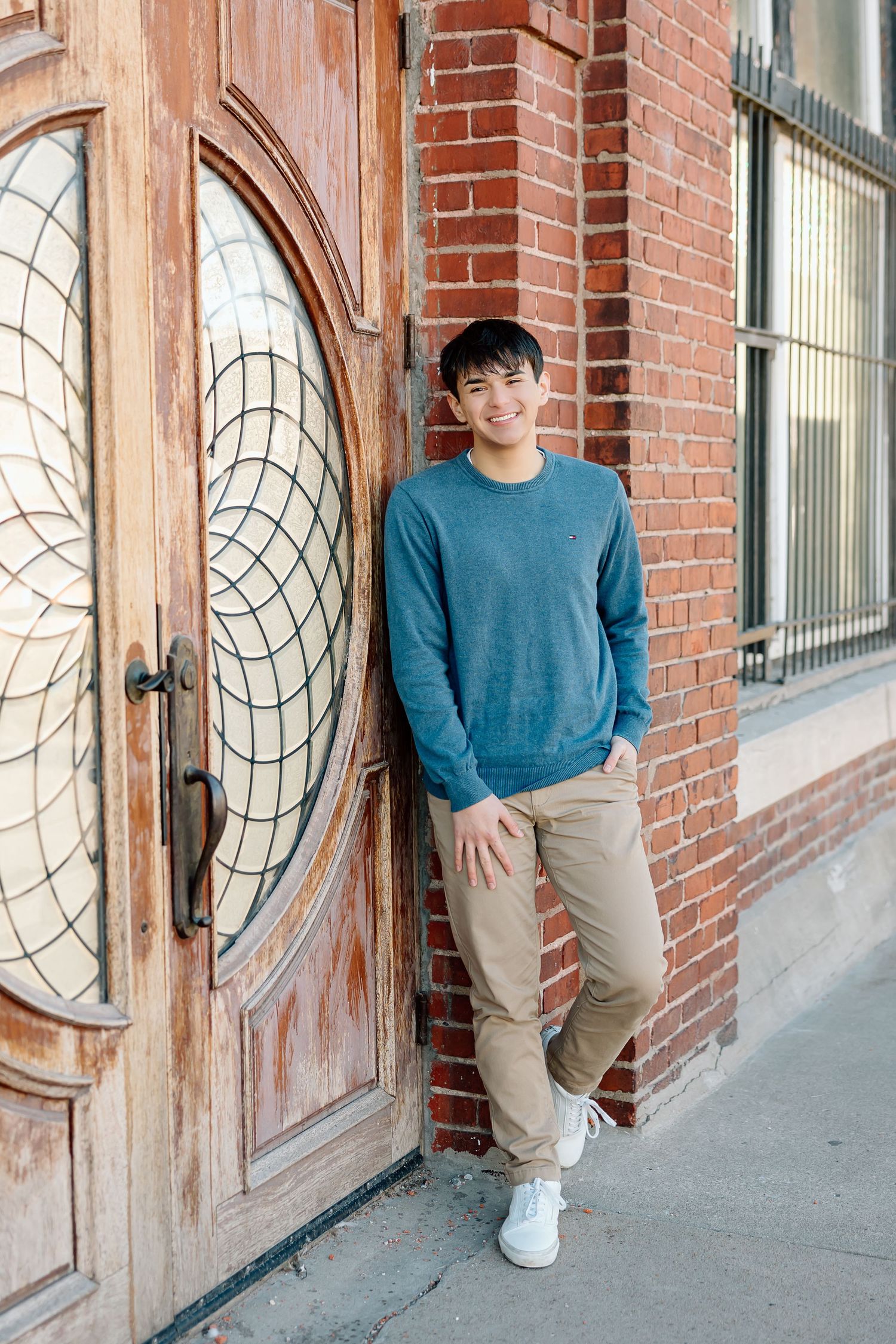 Relaxed pose against brick wall featuring decorative wooden door with circular pattern.