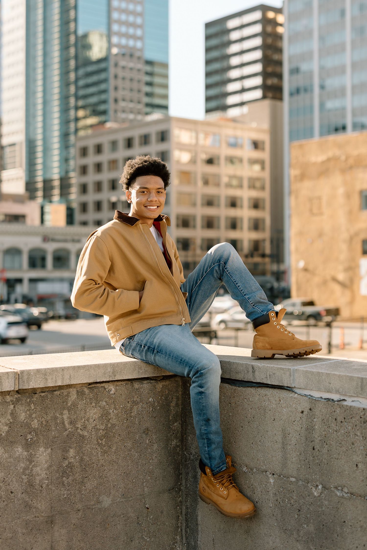 Person in casual attire sits on concrete ledge with urban backdrop.
