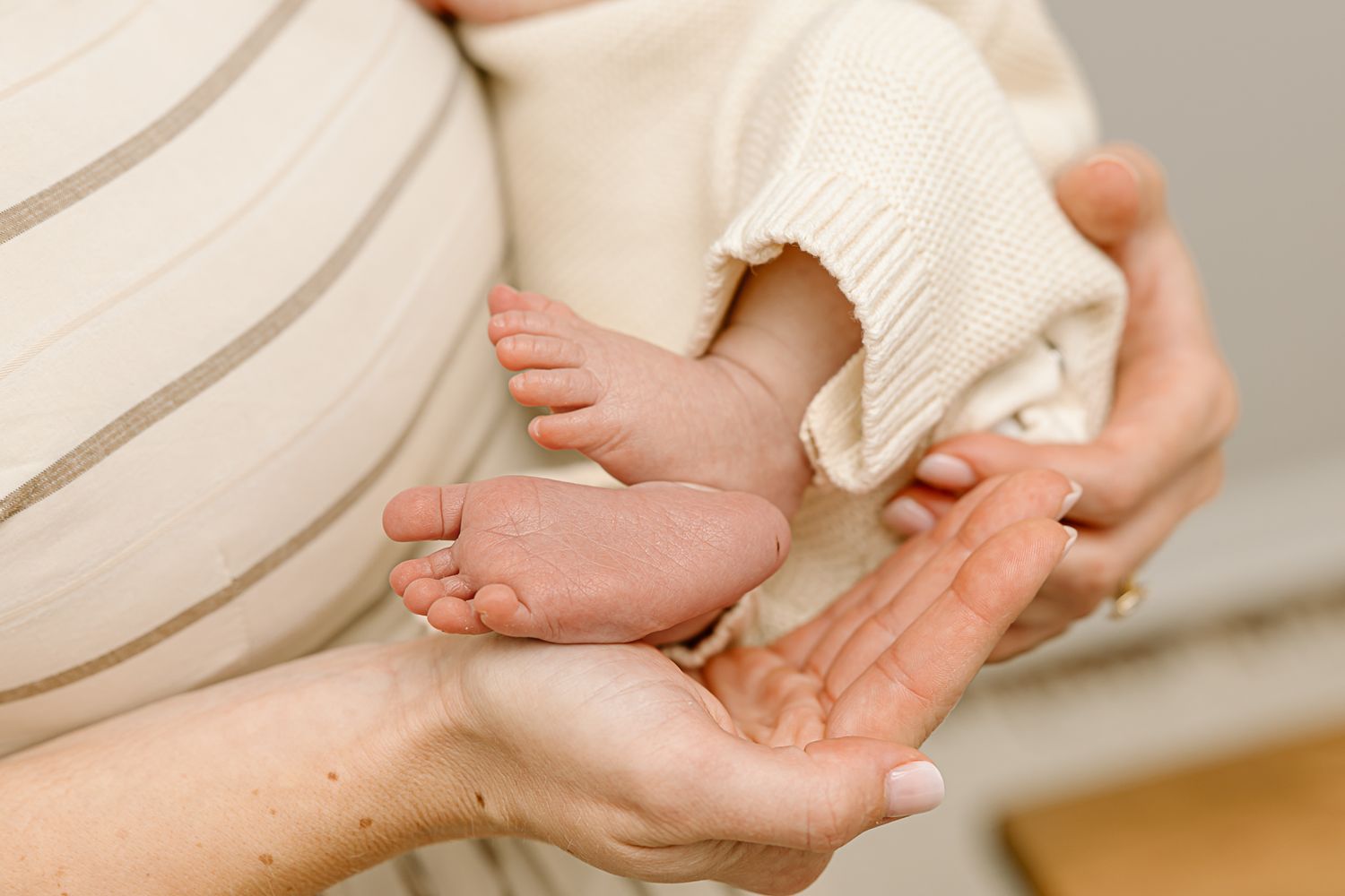 Gentle hands holding tiny newborn feet against cream colored fabric.