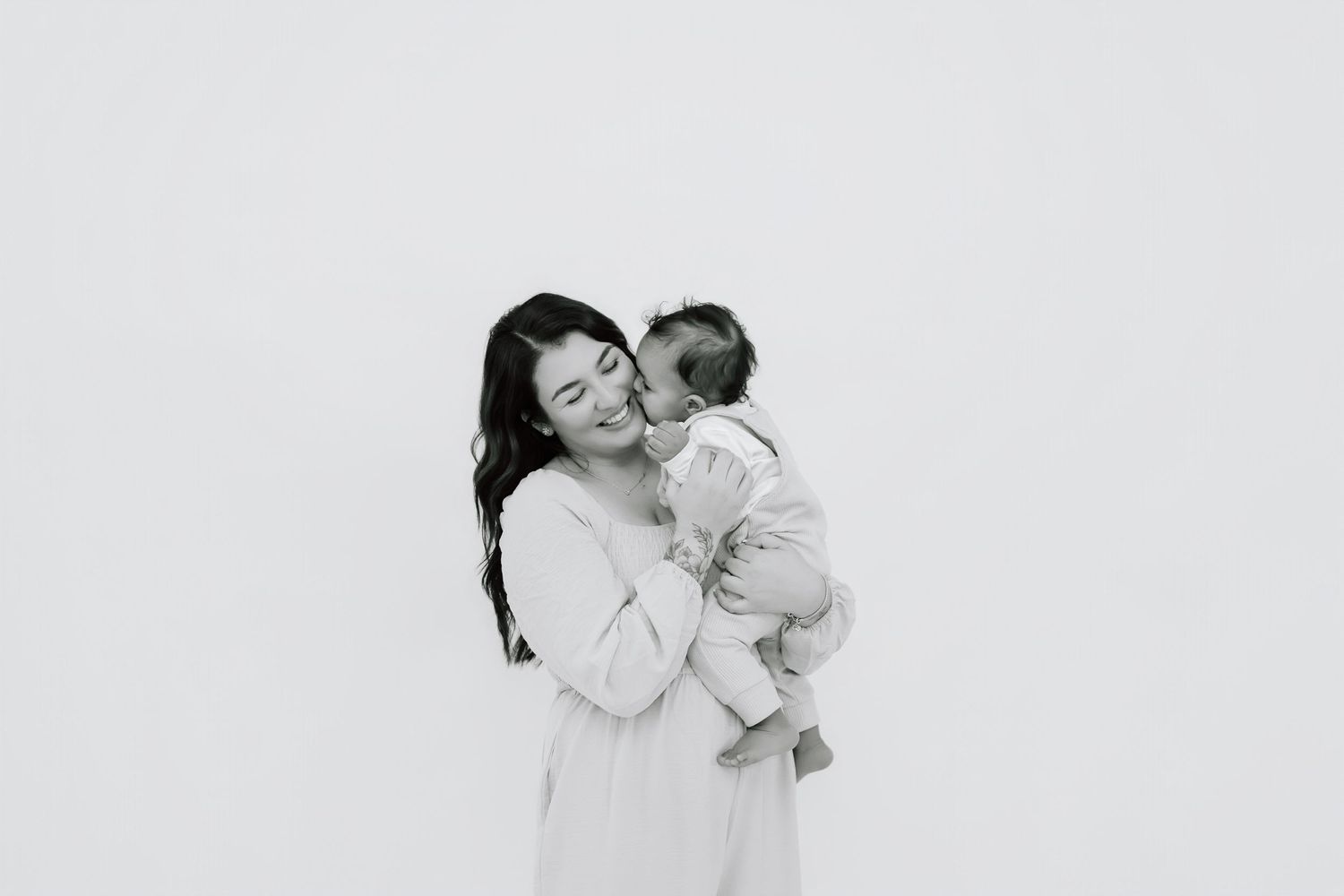 A tender black and white portrait of a parent and baby embracing against a white background.