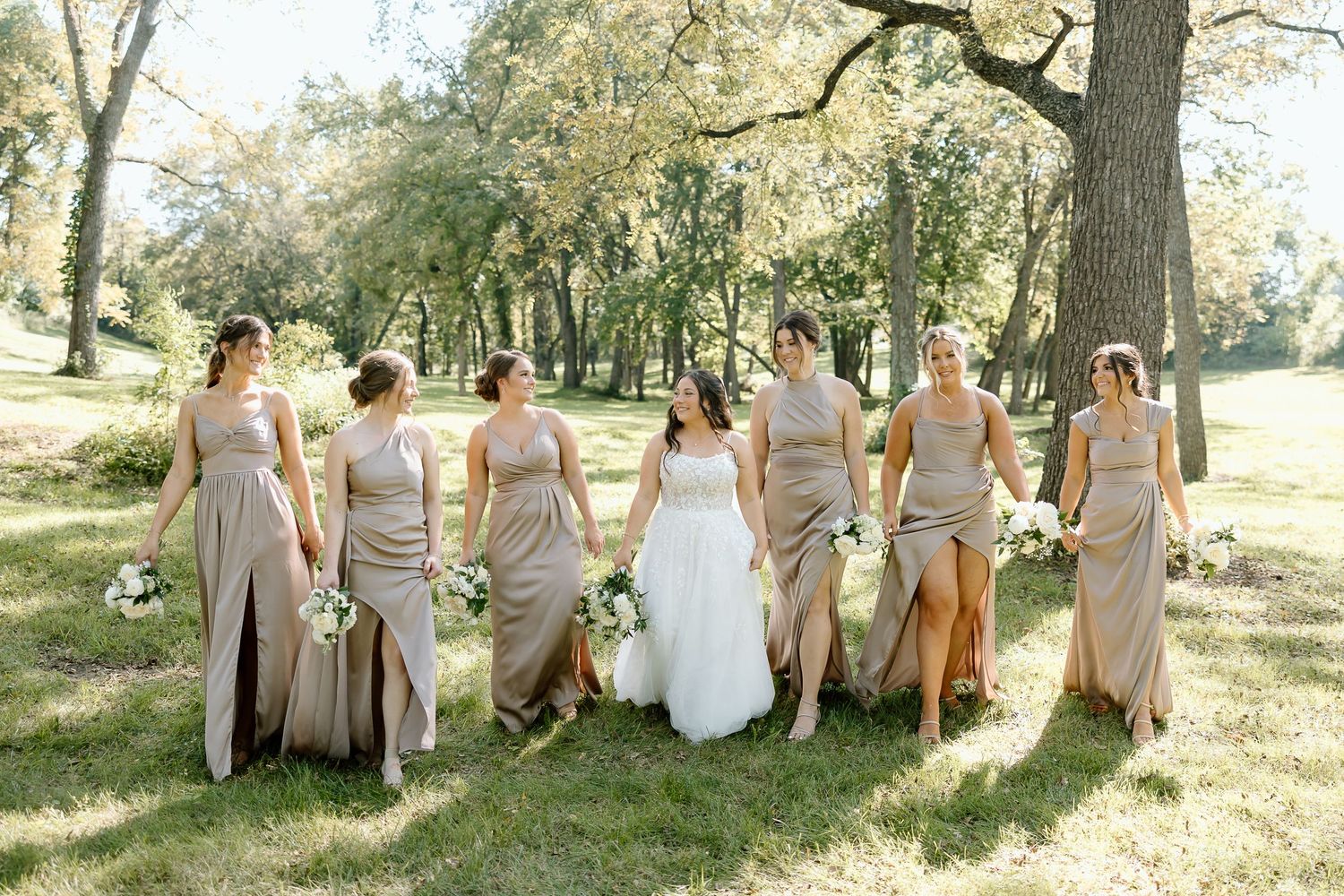 Wedding party in champagne dresses walks together through a sunlit park setting on a beautiful autumn day.