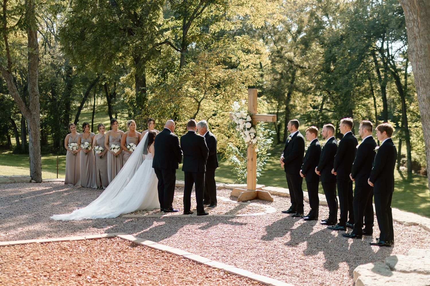 Wedding party stands in a line outdoors during autumn with fallen leaves scattered on the ground.