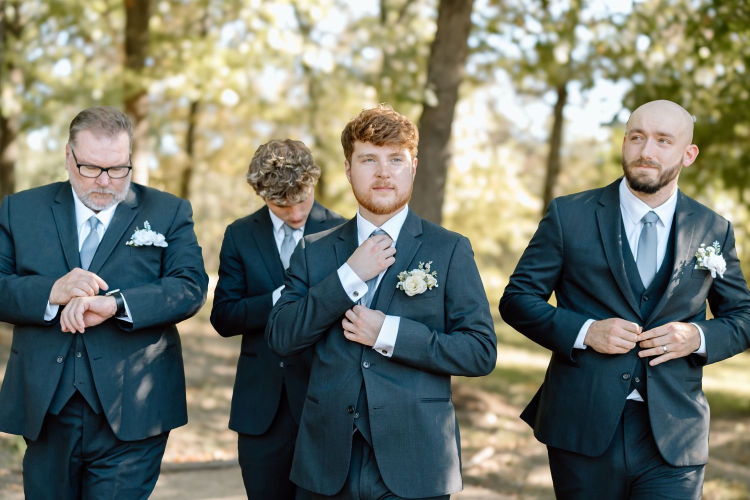 Groomsmen in navy suits playfully pose together outdoors during a wedding photoshoot.