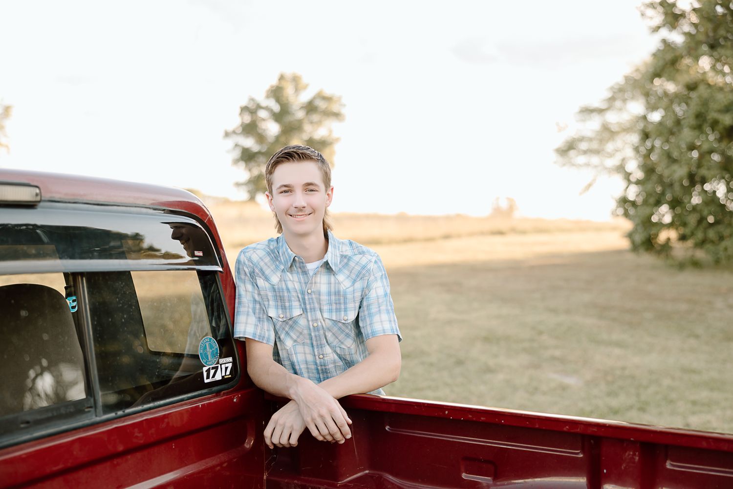 Sunset portrait with someone posing against a red vintage truck in a rural setting.