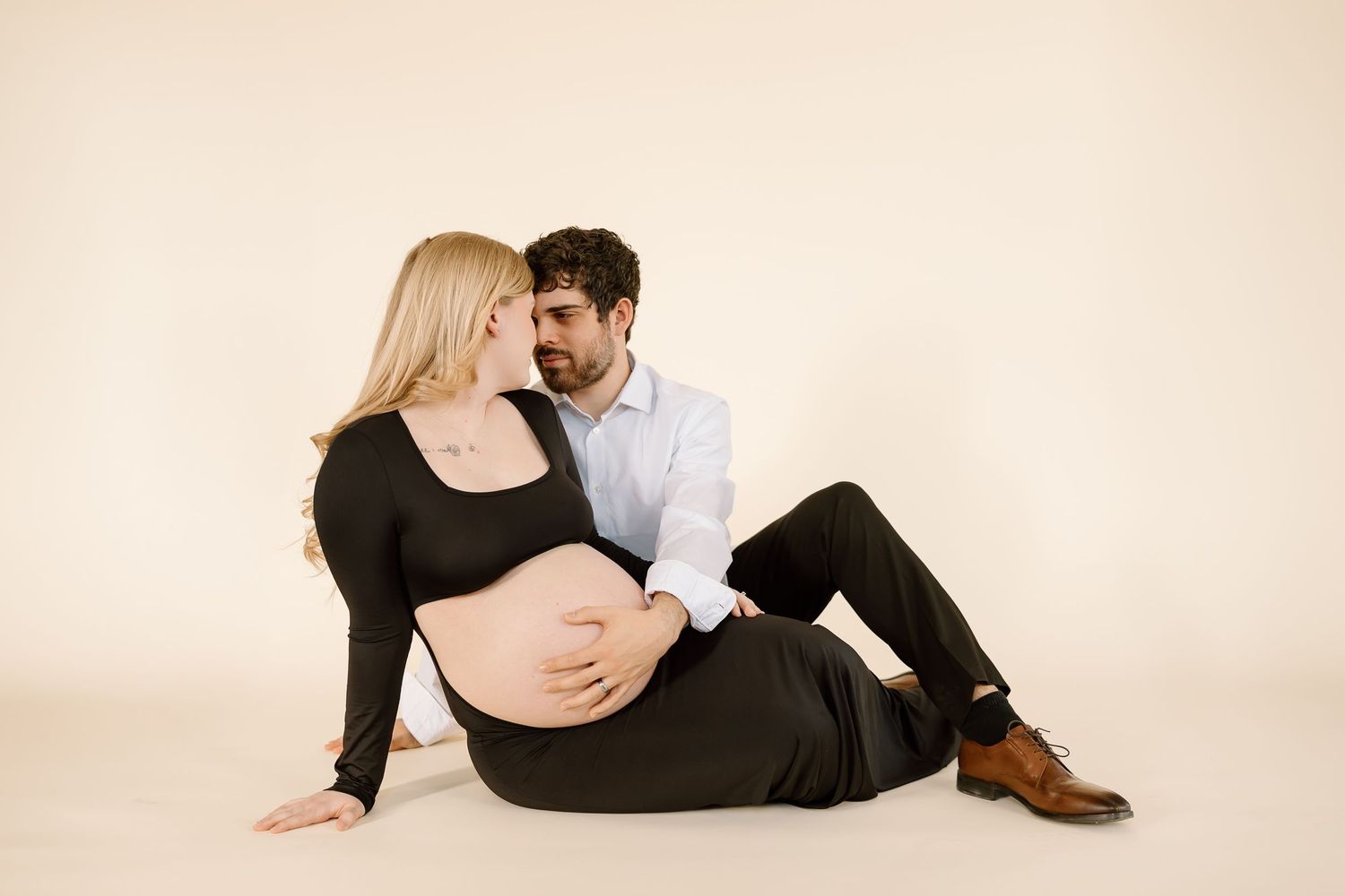 Intimate maternity portrait of couple embracing on cream colored background.
