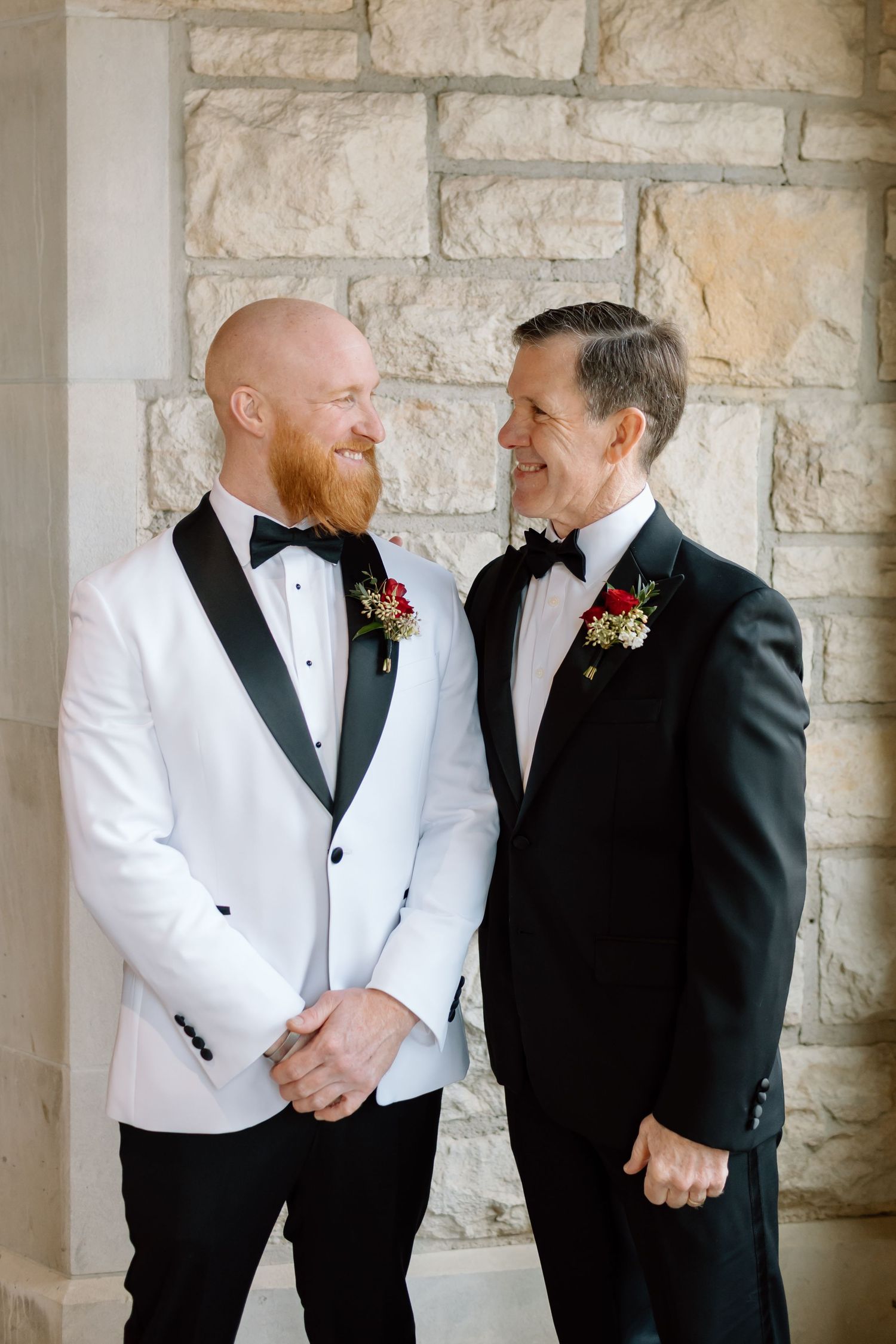 Two people in formal attire share joyful moments together against a stone wall background.