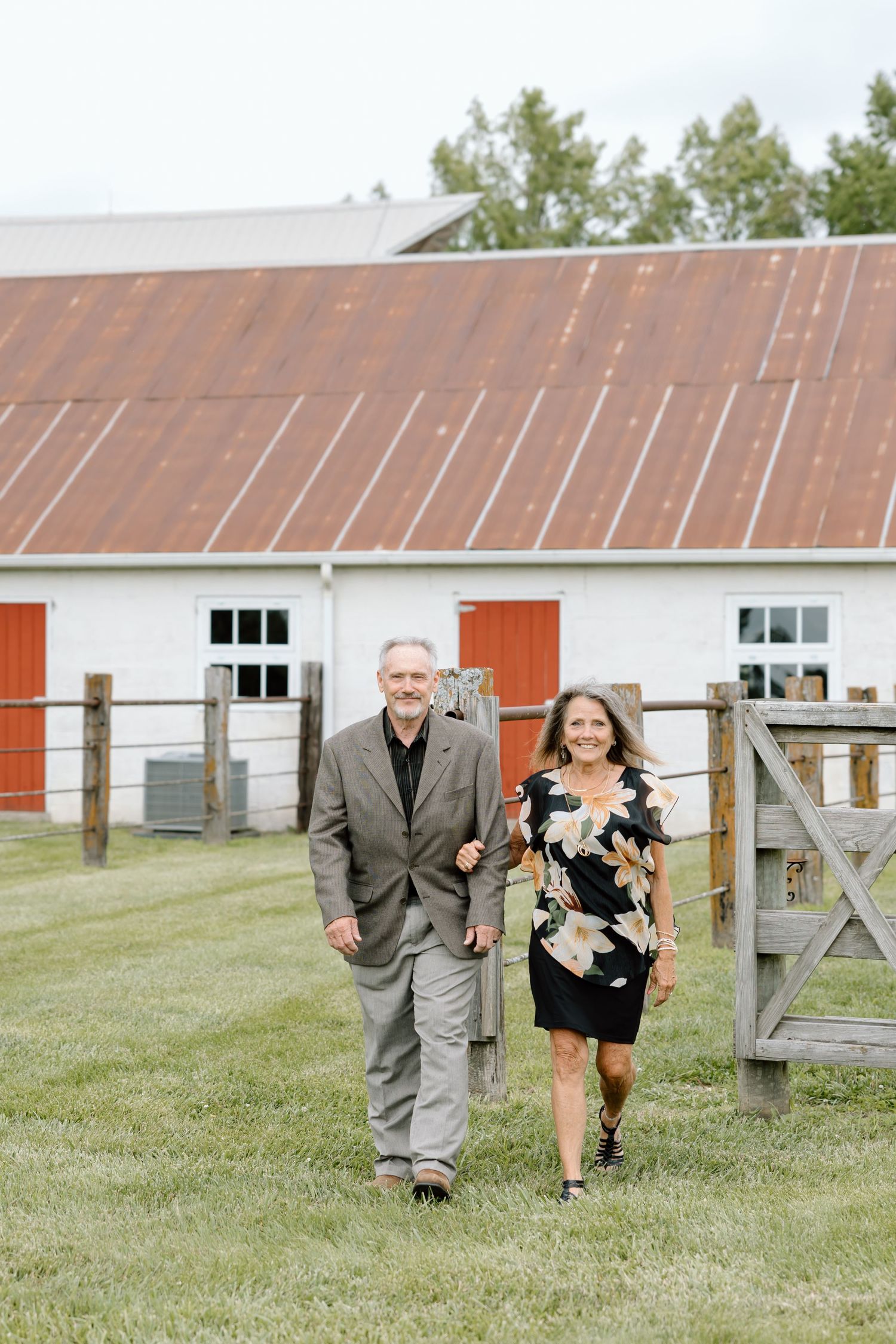 Elderly couple walking hand in hand on a farm with a white barn and red doors in the background.