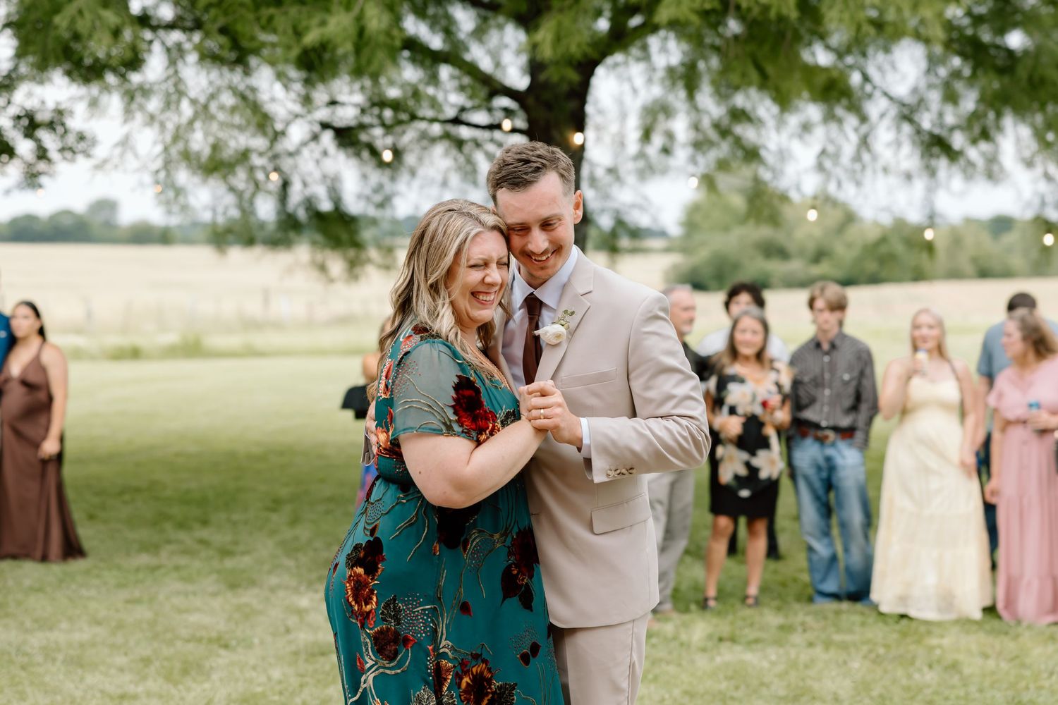 A couple shares a joyful dance outdoors at a wedding reception with guests watching in the background.