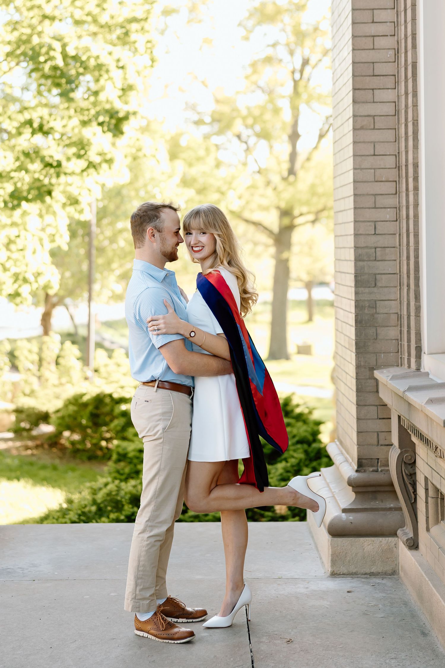 Couple sharing a romantic moment on a columned porch with soft natural lighting and brick walls.