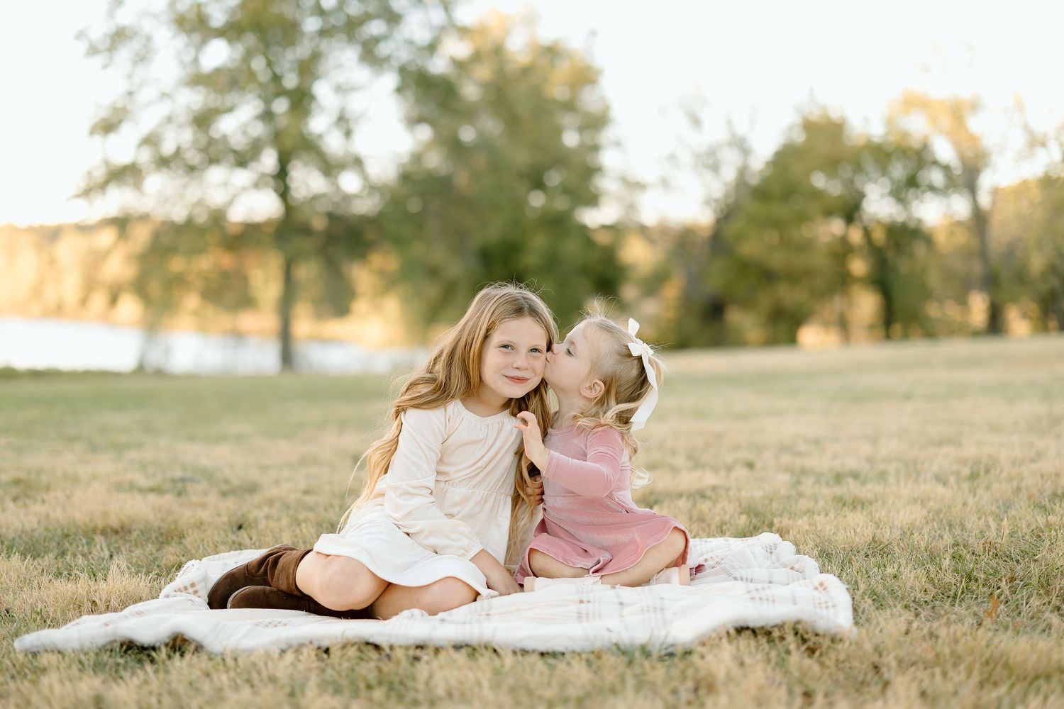 Couple lying on white blanket in grassy field at sunset during romantic outdoor photo session.