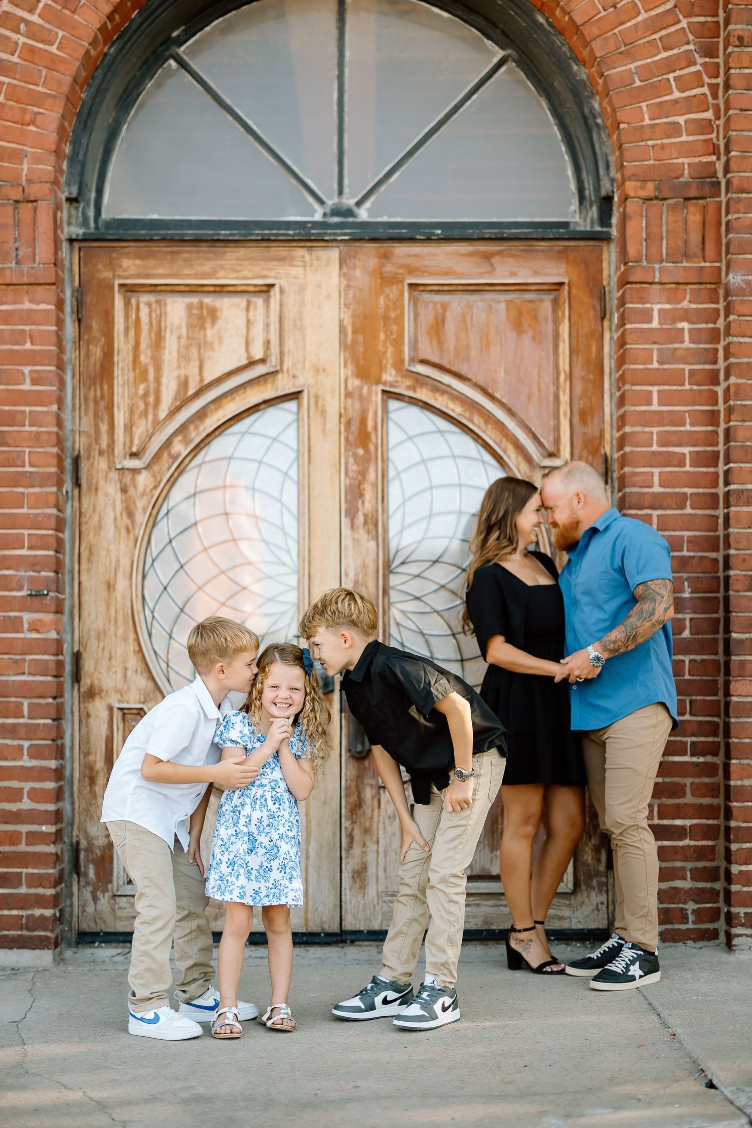 A series of people bending down to peek through arched windows in a brick building facade.