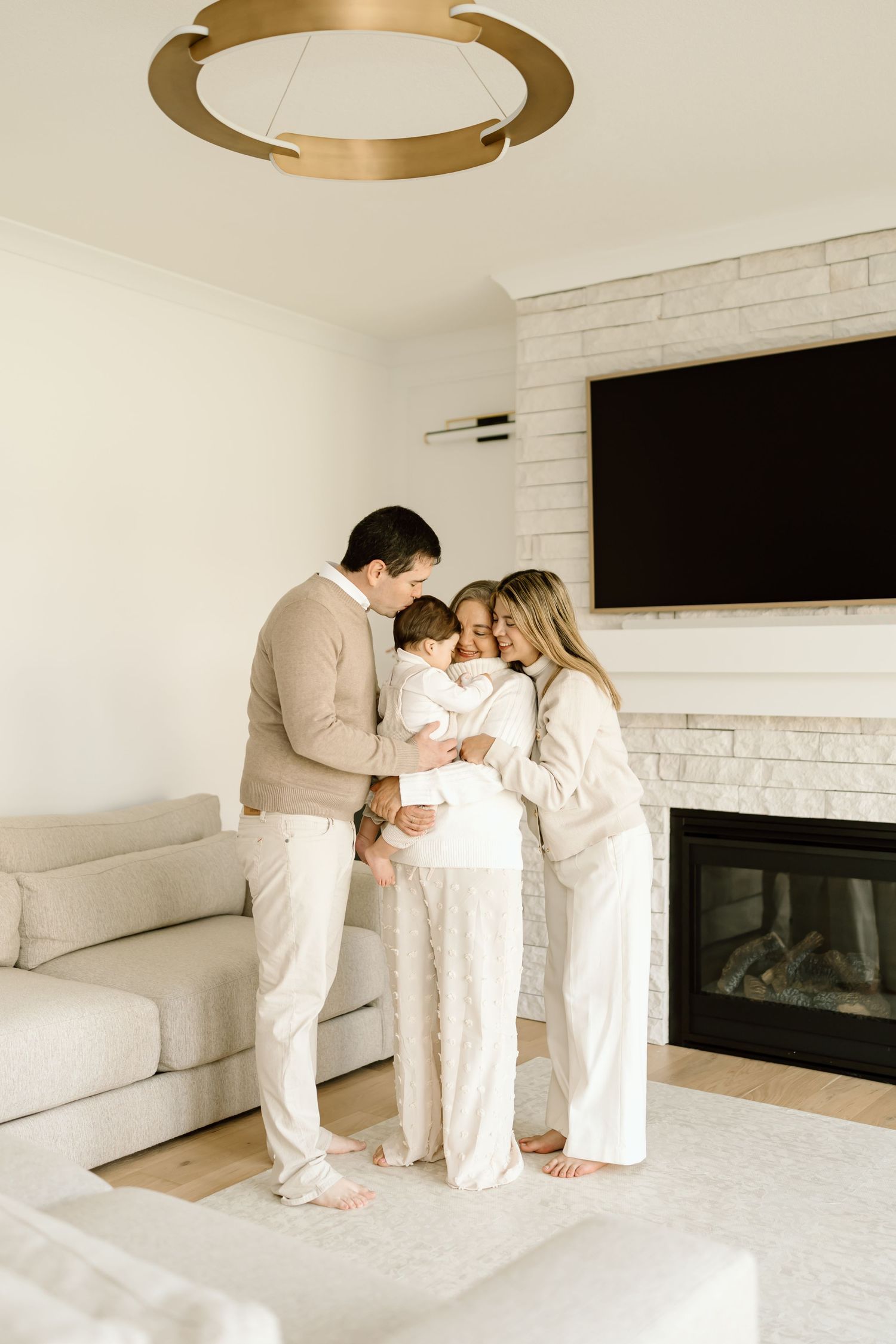 Family wearing white outfits shares tender moments together in a minimalist living room with white brick fireplace.