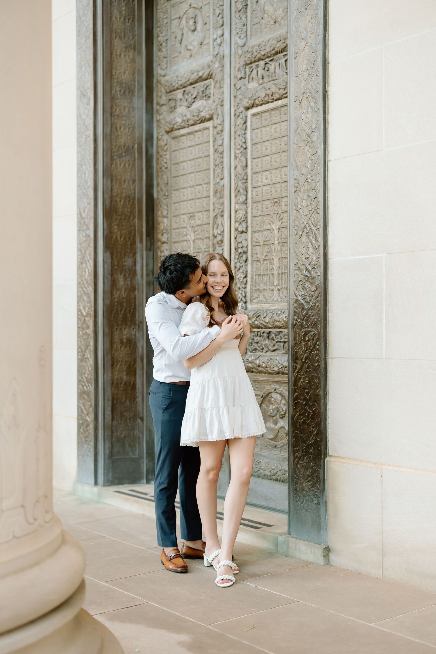 A couple embraces in front of ornate carved stone doors at a historic building entrance.